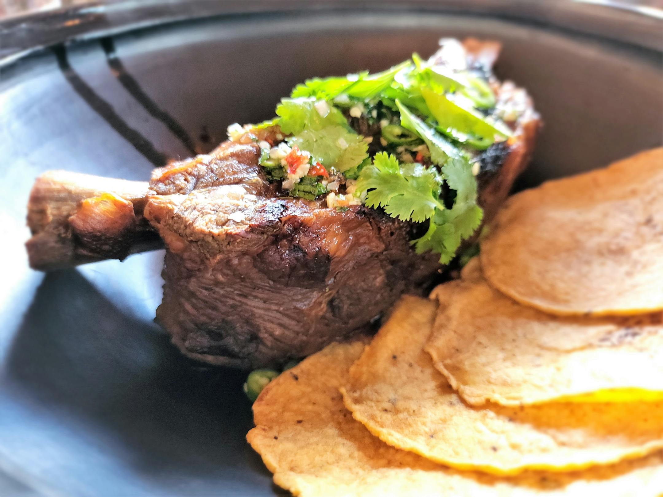 Closeup of a beef long rib and tortillas in a black bowl.