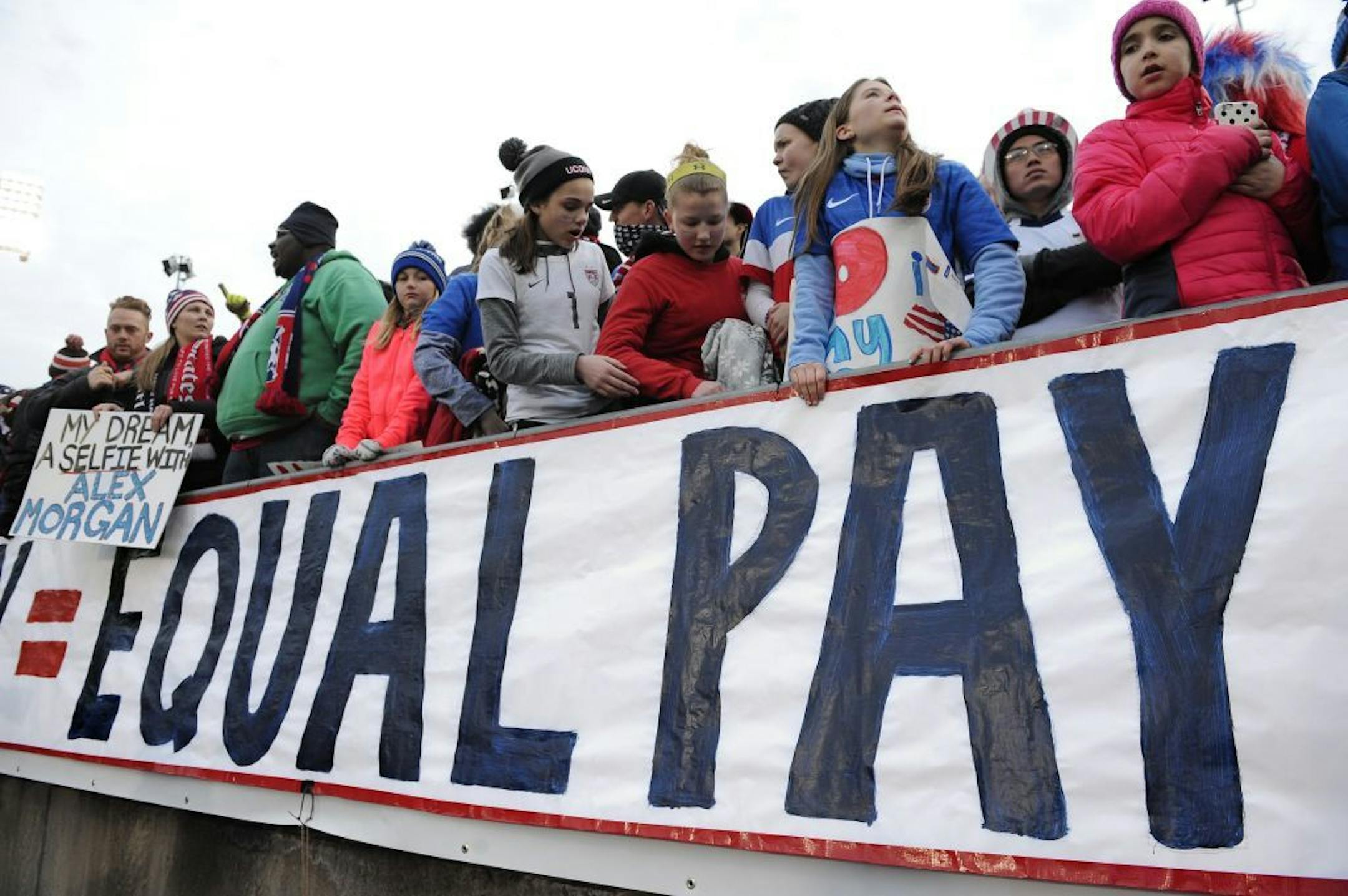 Fans stand behind a large sign for equal pay for the women's soccer team during an international friendly soccer match between the United States and Colombia at Pratt & Whitney Stadium at Rentschler Field, Wednesday, April 6, 2016, in East Hartford, Conn.