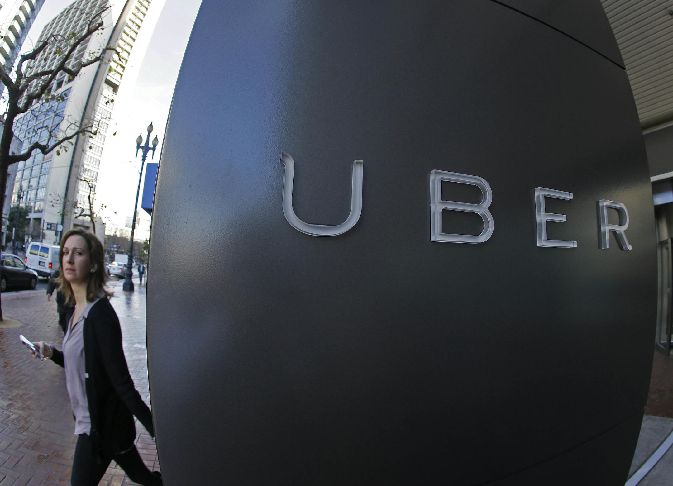 FILE - In this file photo taken Tuesday, Dec. 16, 2014, a woman walks past the company logo of the internet car service, Uber, in San Francisco, USA. Uber&#xed;s chief executive ordered an urgent investigation Monday Feb. 20, 2017, into a sexual harassment claim made by a female engineer who alleged her prospects at the company evaporated after she complained about advances from her boss. (AP Photo/Eric Risberg, FILE)