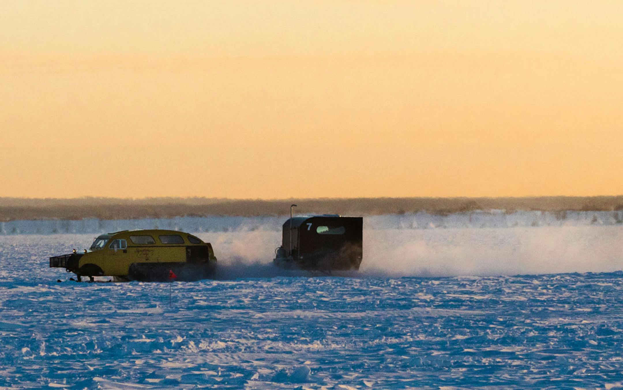 A bombardier cruises across the ice during sunrise on Lake of the Woods. The vehicles are equipped with tracks in the rear and skis in the front to make it easier to traverse snow drifts on the ice.