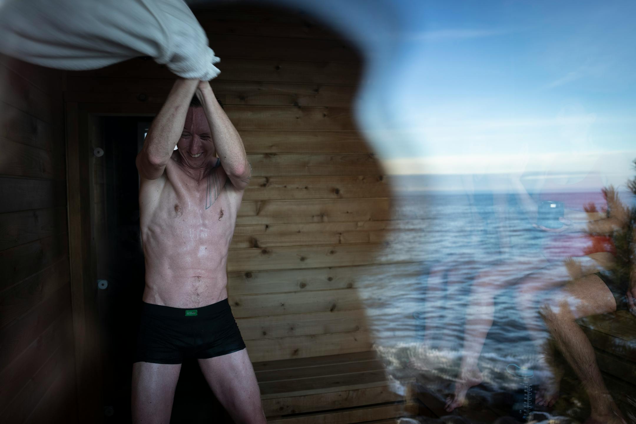 Shaun Tudor swings a towel around to move the air while another sauna participant paddles water onto the rocks to generate steam while enjoying a sauna session at Sisu and Löyly Sauna.
