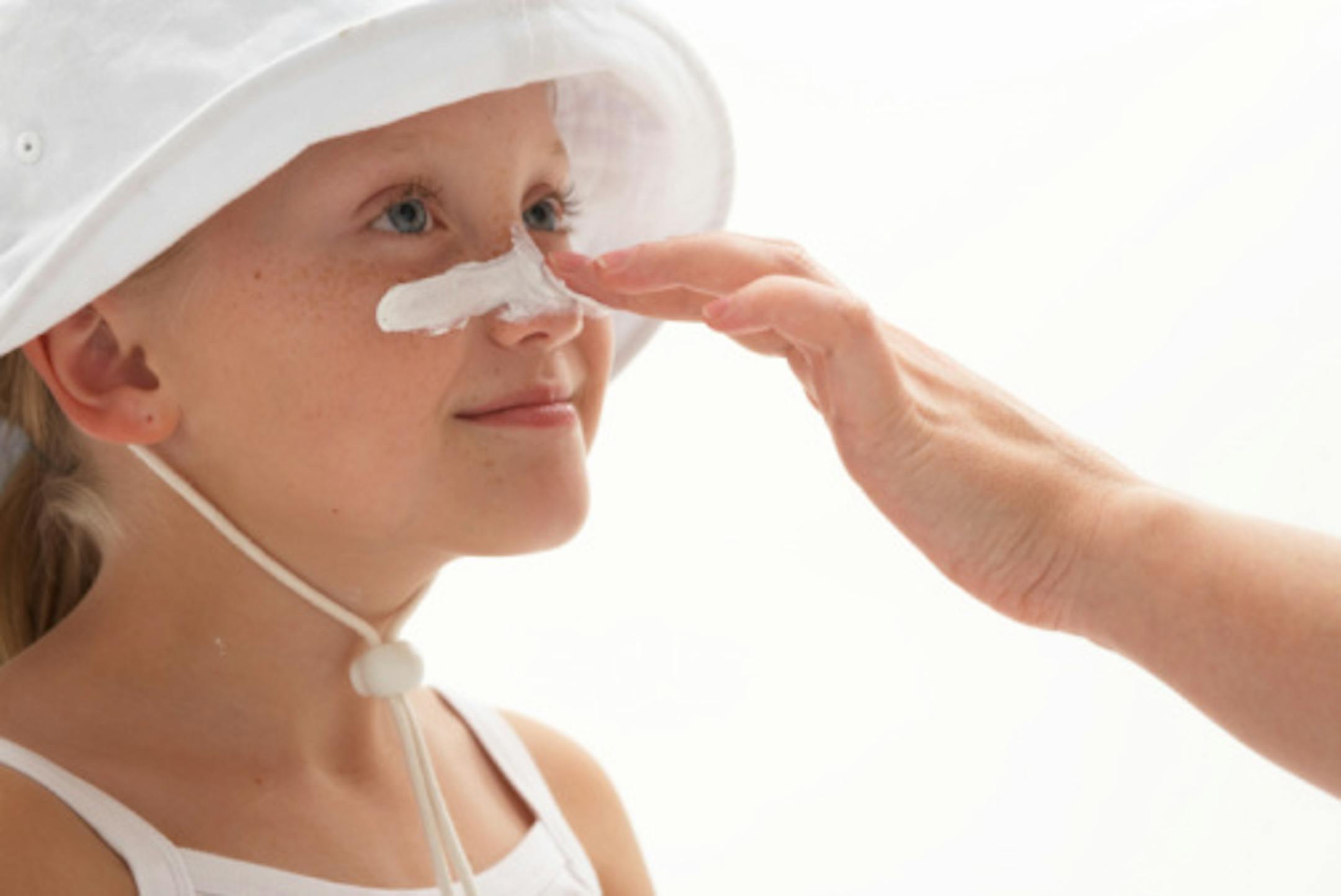 Girl (7-9) having sun cream applied to nose