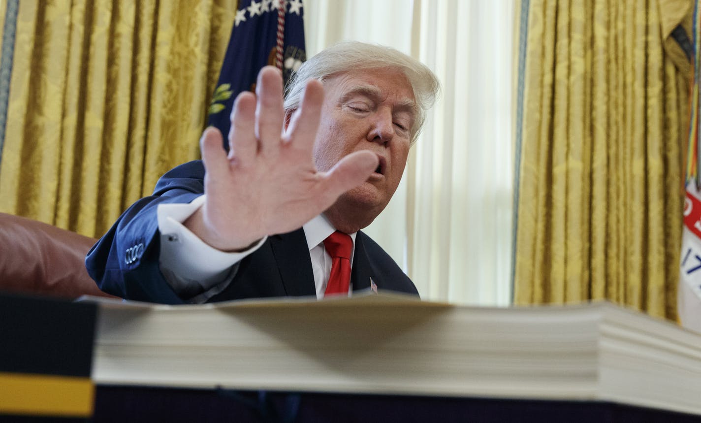 President Donald Trump places his hand over the tax bill before signing it in the Oval Office of the White House, Friday, Dec. 22, 2017, in Washington. (AP Photo/Evan Vucci)