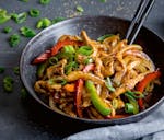 A wok with chicken and bell pepper stir-fry and topped with green onions, which makes for a quick and easy dinner.