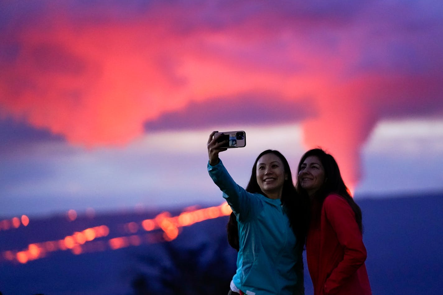 Ingrid Yang, left, and Kelly Bruno, both of San Diego, take a photo in front of lava erupting from Hawaii's Mauna Loa volcano Wednesday, Nov. 30, 2022, near Hilo, Hawaii. (AP Photo/Gregory Bull)