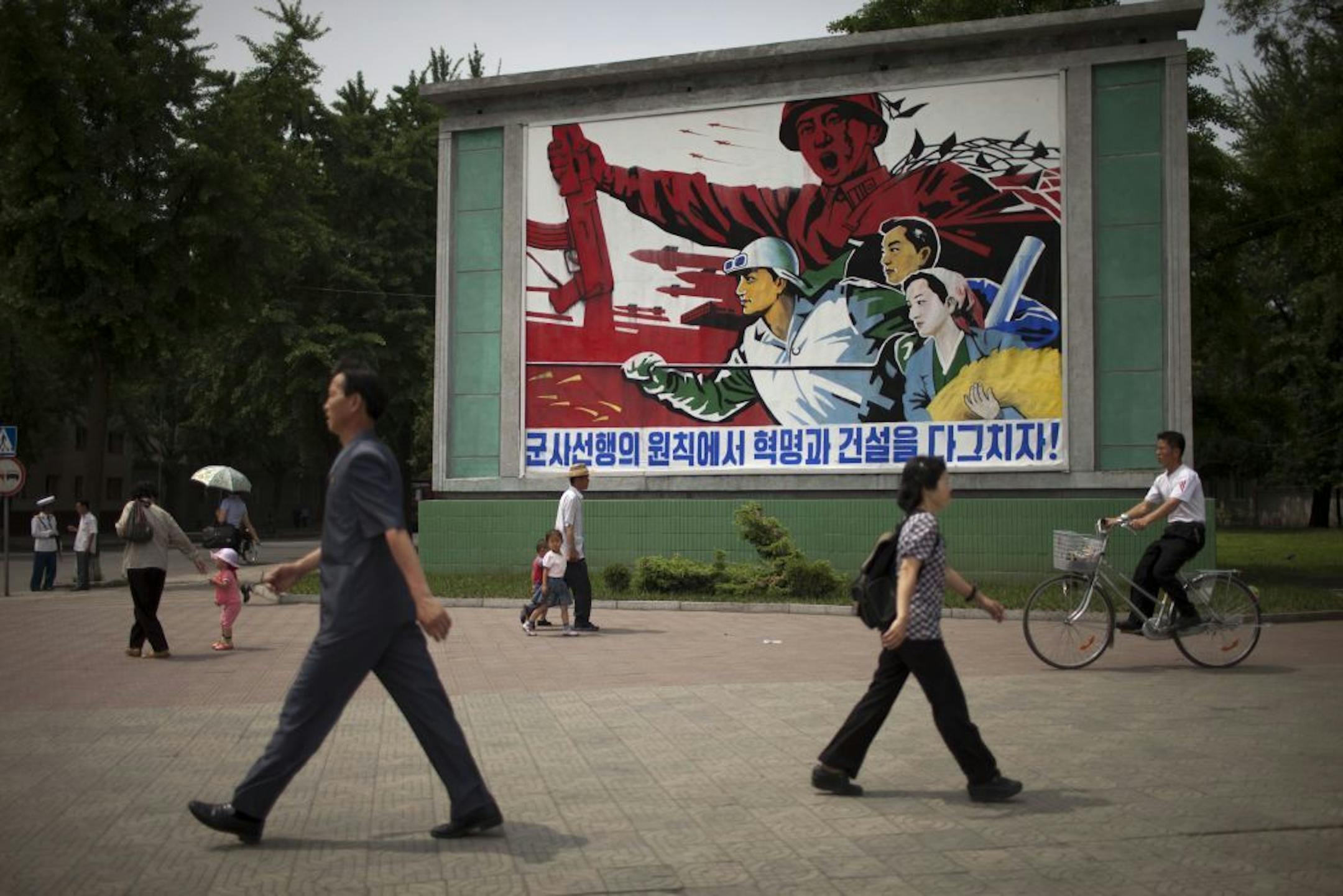 People walk past a roadside propaganda billboard promoting the "military first" policy and a boost to build the country's economy in Pyongyang, North Korea, Sunday, June 16, 2013. North Korea's top governing body on Sunday proposed high-level nuclear and security talks with the United States in an appeal sent just days after calling off talks with rival South Korea.