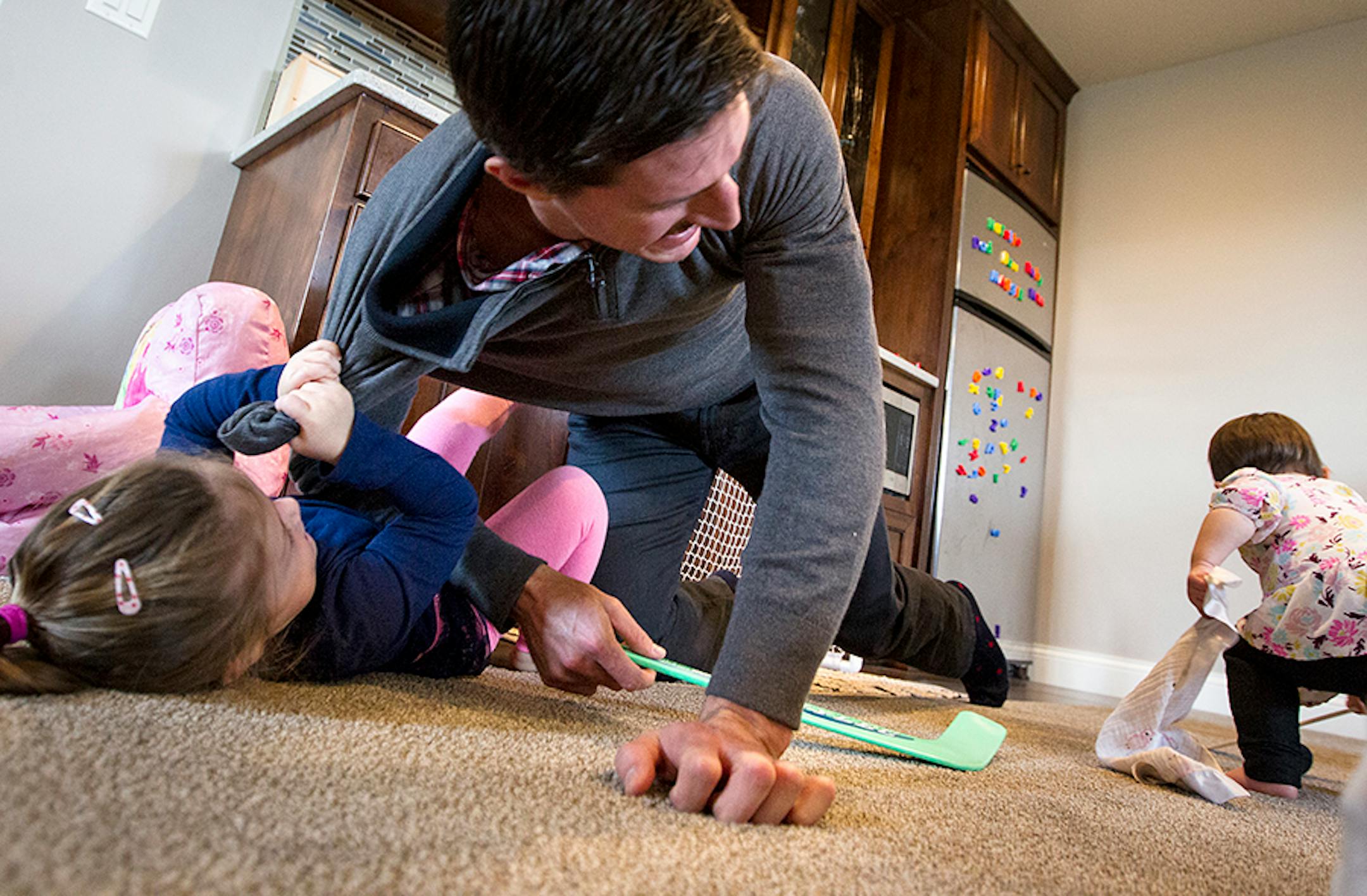 Minnesota Wild's Ryan Carter is taken down by his daughter Maggie, 3, as they play hockey at home in Gem Lake November 22, 2015. Natalie, 15 months, right, is his second daughter, and Ryan and his wife Erin are expecting a third child due next year.