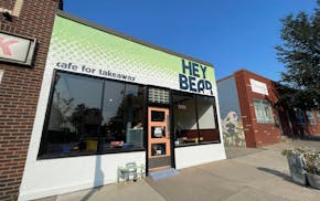 The small outside of the cafe is painted white with a lime green top. There are large windows facing the street and a small, wood framed door.