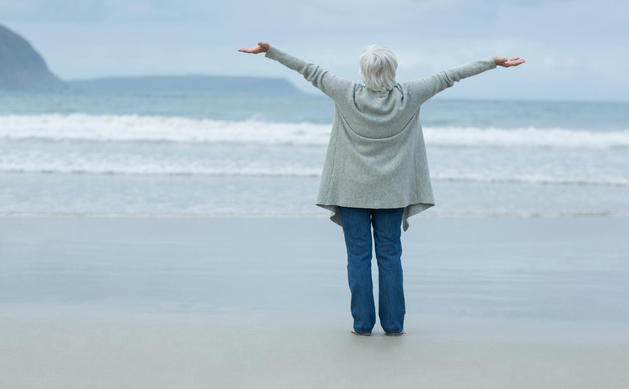 Rear view of mature woman with arms outstretched standing on the beach