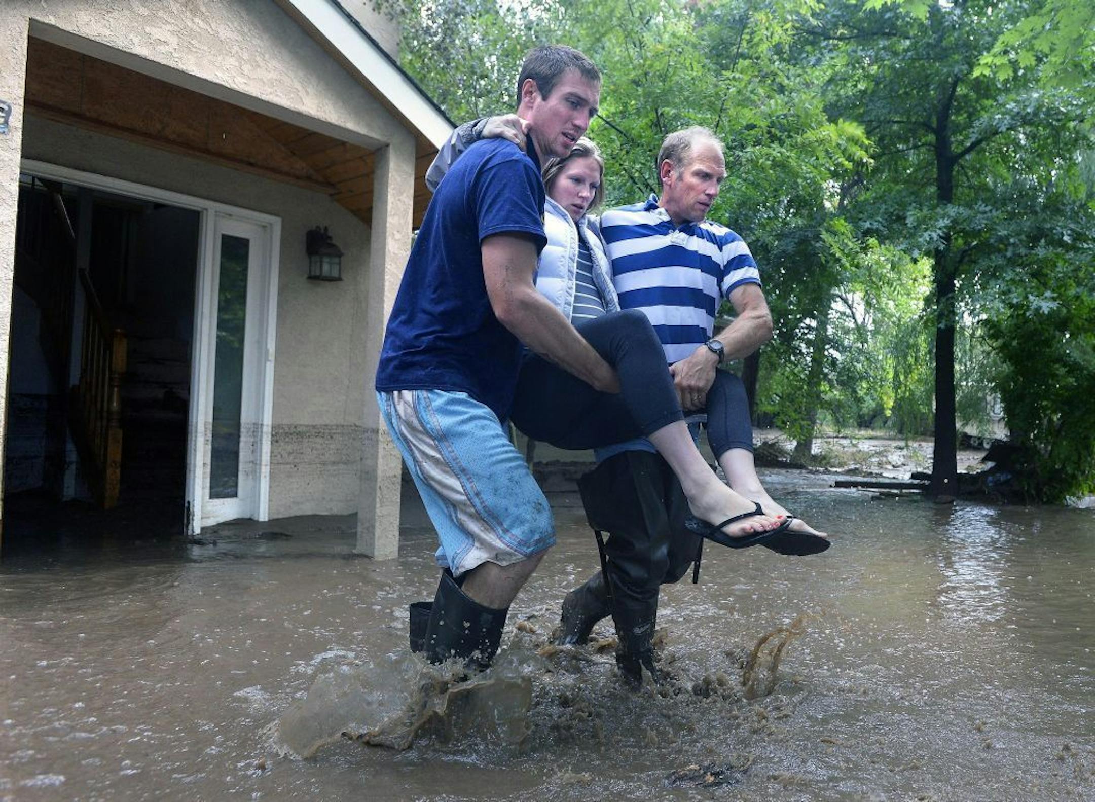 Kyle Schuler, left, carries his pregnant sister with the help of his father Kim Schuler, right, after gathering belongings from their flooded home on Upland Avenue, Friday, Sept. 13, 2013 in Boulder, Colo. By truck and helicopter, thousands of people stranded by floodwaters came down from the Colorado Rockies on Friday, two days after seemingly endless rain turned normally scenic rivers and creeks into coffee-colored rapids that wrecked scores of roads and wiped out neighborhoods. (AP Photo/The