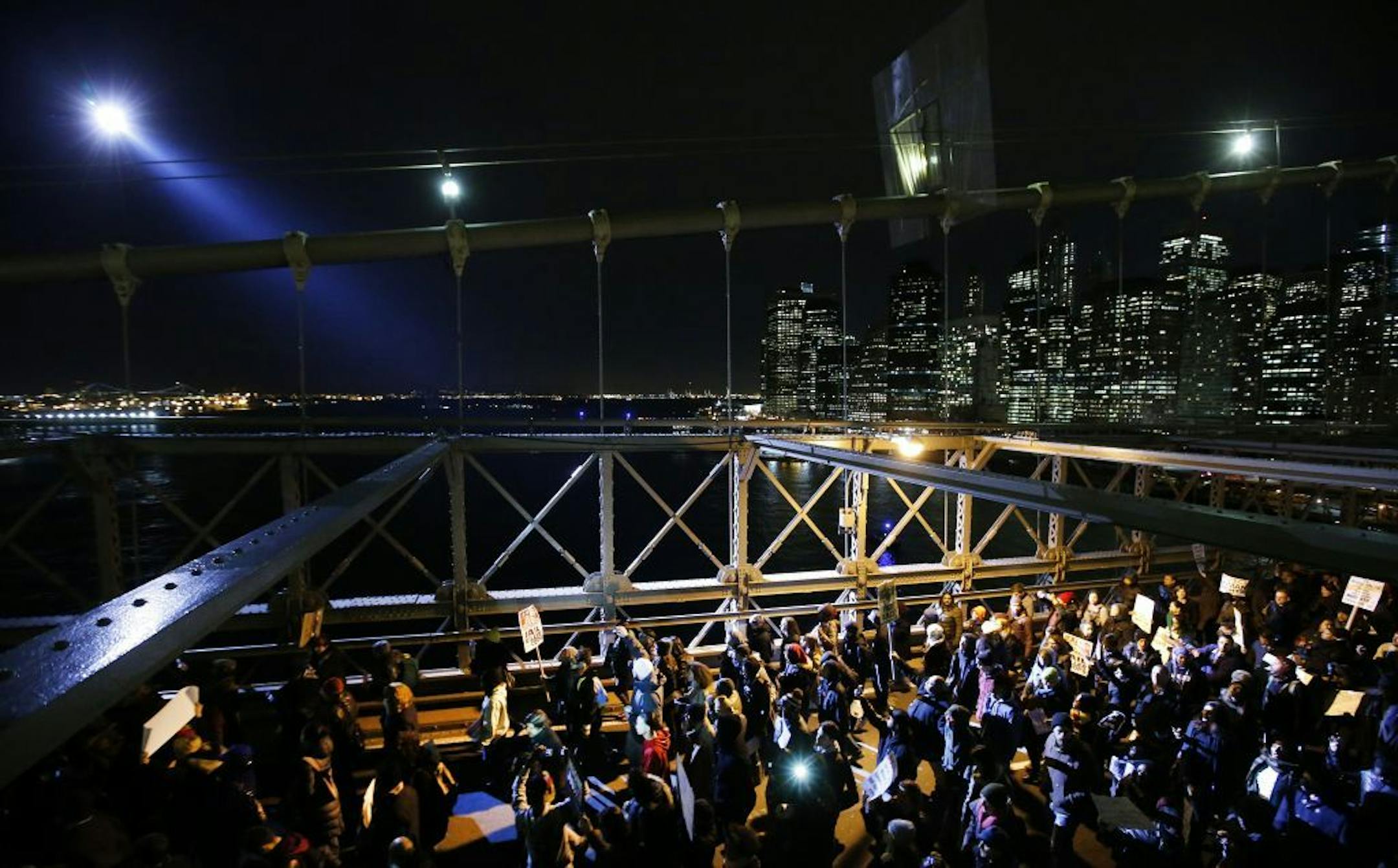 A police helicopter shines a light on protesters rallying against a grand jury's decision not to indict the police officer involved in the death of Eric Garner as they cross the eastbound traffic lanes of the Brooklyn Bridge, Thursday, Dec. 4, 2014, in New York. A grand jury cleared a white New York City police officer Wednesday in the videotaped chokehold death of Garner, an unarmed black man, who had been stopped on suspicion of selling loose, untaxed cigarettes.