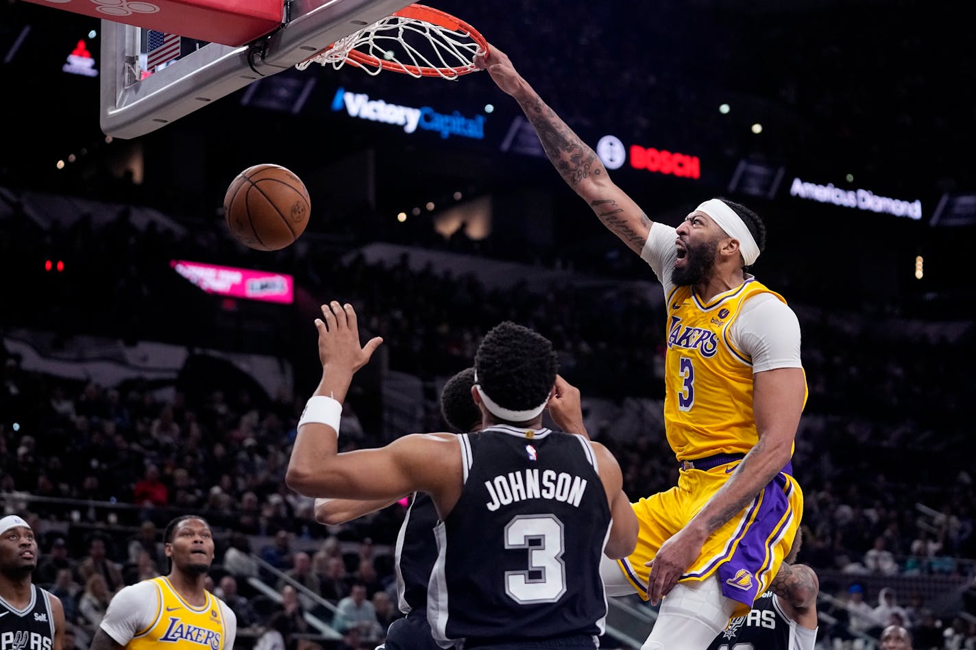 Los Angeles Lakers forward Anthony Davis (3) reacts as he scores over San Antonio Spurs center Victor Wembanyama (1) and forward Keldon Johnson (3) during the first half of an NBA basketball game in San Antonio, Wednesday, Dec. 13, 2023. (AP Photo/Eric Gay)