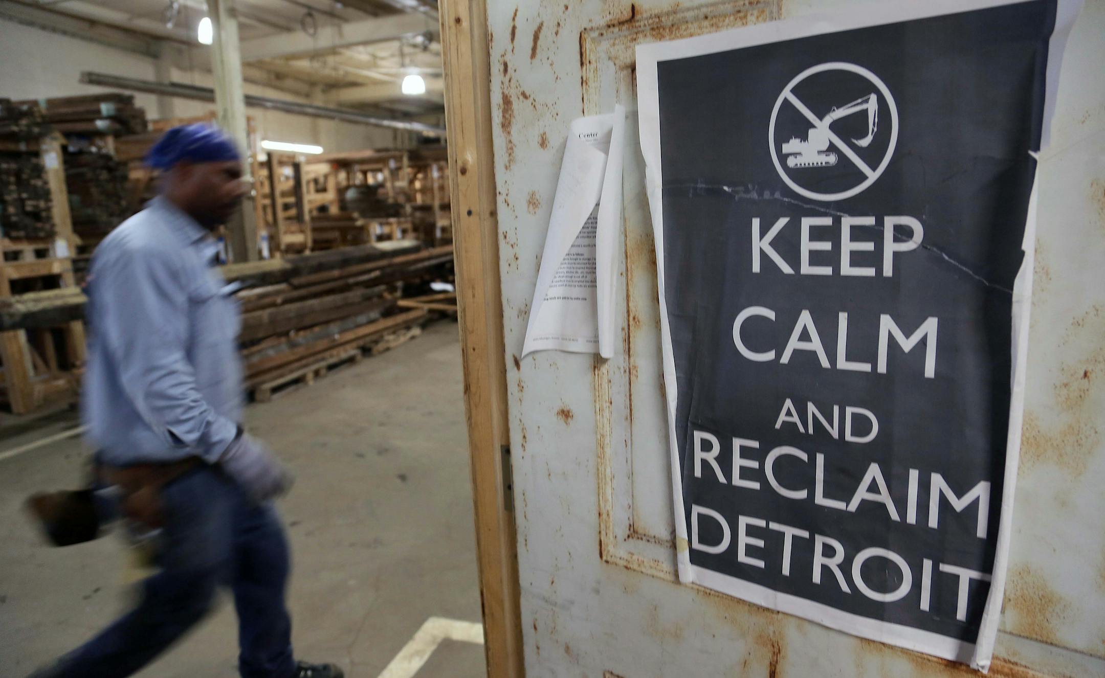 ADVANCE FOR SUNDAY MARCH 31 - In this Feb. 28, 2013 photo, John Binion, 41, of Detroit walks by a poster at the Reclaim Detroit warehouse in Detroit where workers salvage wood and other household items that were taken from abandon homes in Detroit and making them useful for other projects. (AP Photo/Detroit Free Press, Mandi Wright) DETROIT NEWS OUT; MAGS OUT; NO SALES ORG XMIT: MIDTF107