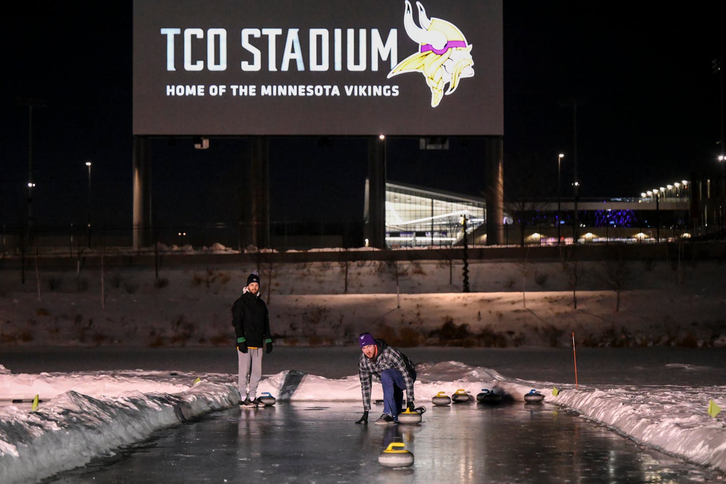 Mitch Perila, center, and Rob Norton, of Bloomington, practice their stone throwing during the USA Curling Experience at Winter Skolstice Friday, Jan. 28, 2022 at the pond between the TCO Performance Center and Omni Viking Lakes Hotel in Eagan, Minn. Team USA curling moved its headquarters from Stevens Point, Wis., to the new Vikings complex in Eagan last April, and several teams train at the facility there. They also have a new CEO. The organization has evolved from a mom-and-pop operation to a modern Olympic governing body since the USOC threatened to strip its accreditation in 2014 after poor Olympic results.