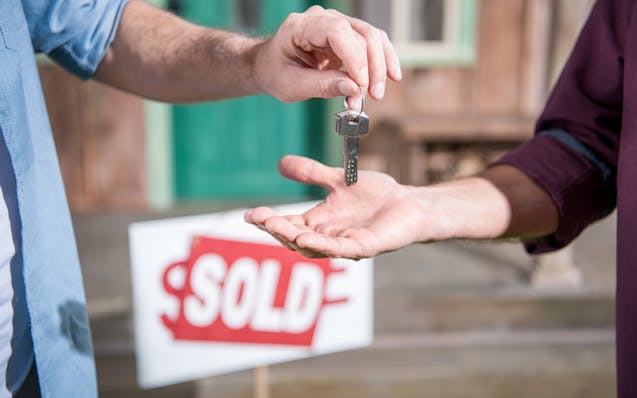 cropped view of man buying new house and taking keys, sold sign behind