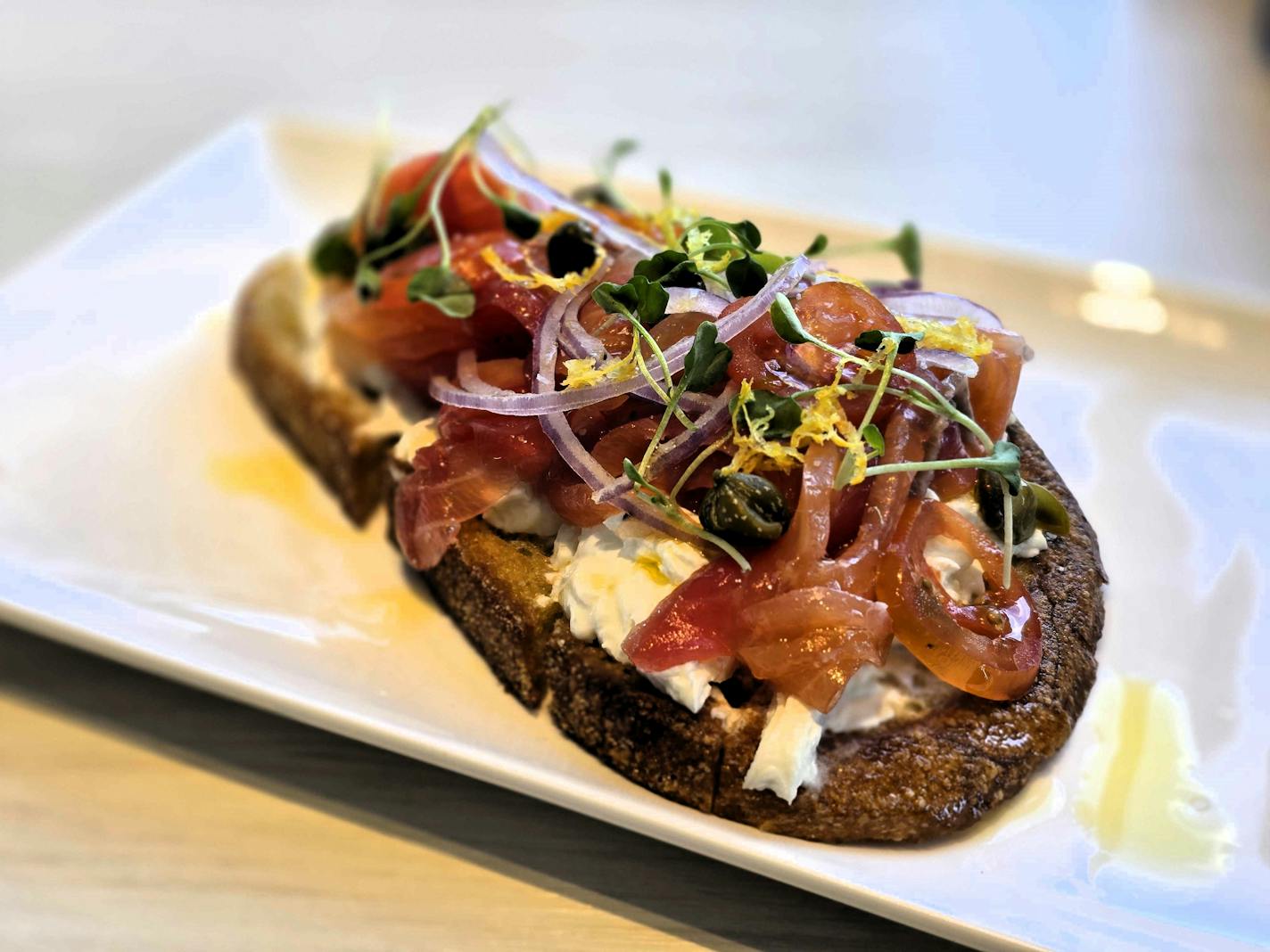 Slice of sourdough with cream cheese and piles of ruby red gravlax and shaved red onion