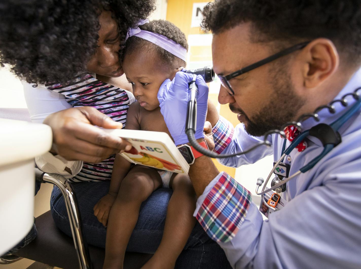 Dr. Nathan Chomilo checks the ears of 15-month-old Tedra Gbelia during her well-child visit as her mother Lorpu Cyrus distracts her with the book she just received. ] LEILA NAVIDI &#xef; leila.navidi@startribune.com BACKGROUND INFORMATION: Dr. Nathan Chomilo sees 15-month-old Tedra Gbelia for a well-child visit with her mother Lorpu Cyrus at Park Nicollet Clinic in Brooklyn Center on Friday, July 13, 2018.