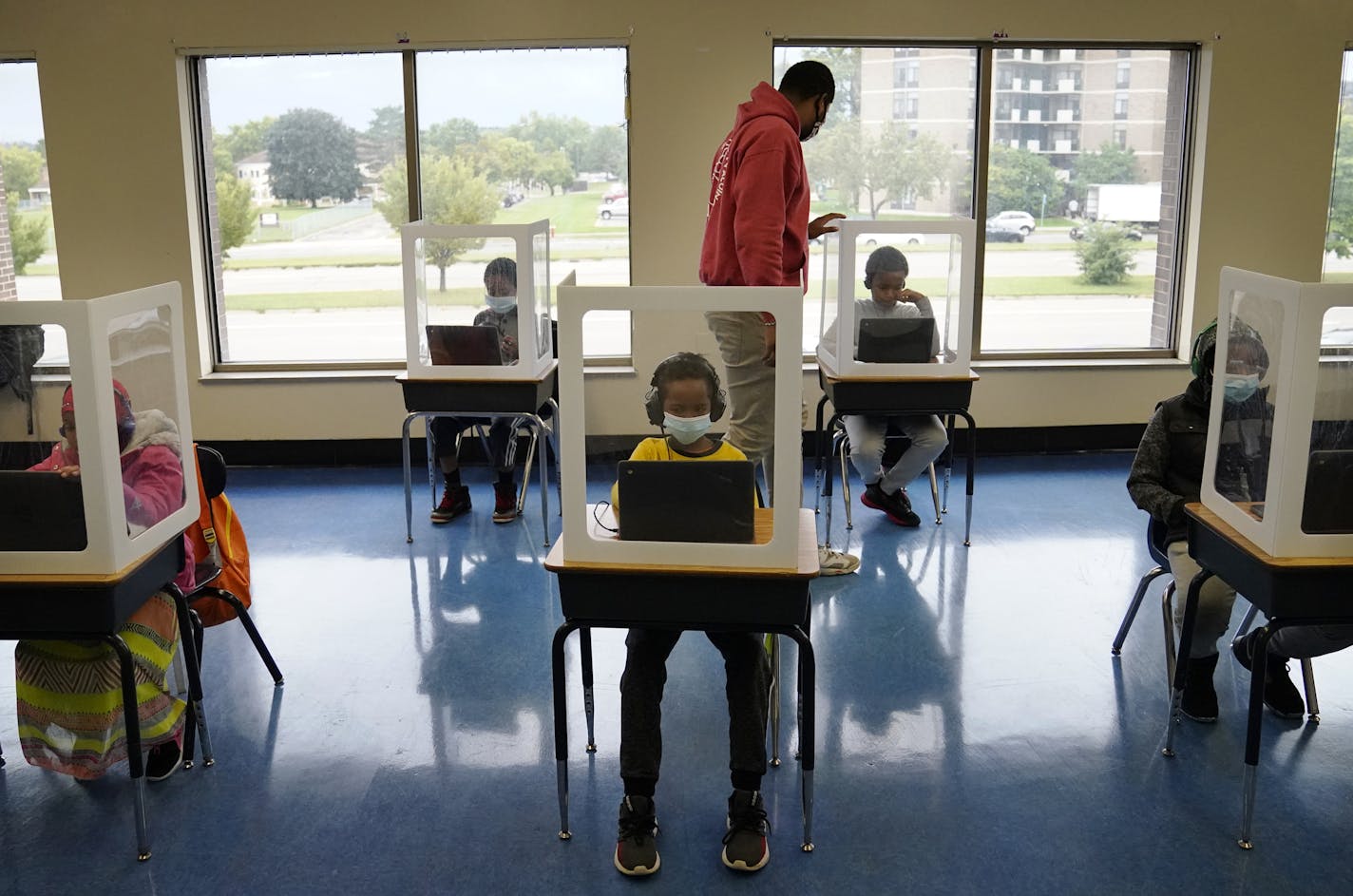 It was back to school for some students at Harvest Best Academy Tuesday in Minneapolis, but with masks, plastic barriers and other new precautions in the era of COVID-19. Here, para professional Jaevon Walton, middle, reminded a student to wear his face mask in a learning pod of 2nd through 7th graders. ] DAVID JOLES • david.joles@startribune.com Tuesday, Sept. 8, 2020, in Minneapolis, MN Students in masks, distance learning, teachers talking to cameras in empty classrooms, lessons in tents and