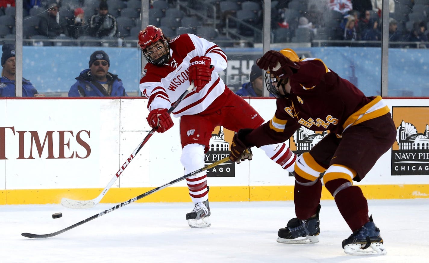 Wisconsin forward Tyler Barnes, left, shoots past Minnesota defenseman Seth Helgeson during the first period of a college hockey game at Chicago's Soldier Field