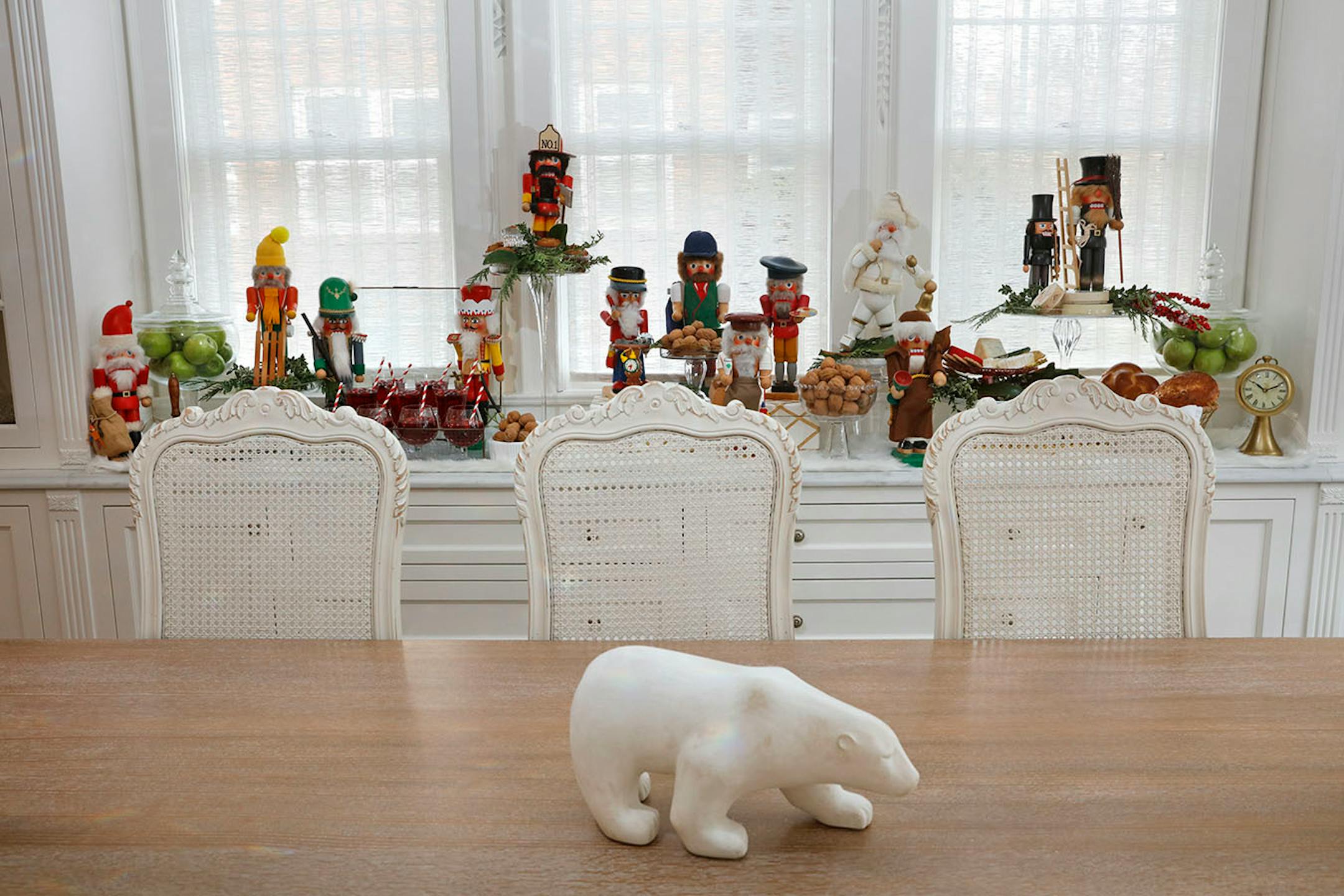 Nutcracker Suite: Display a nutcracker collection on a dining room buffet table. Place some of the nutcrackers on clear glass cake stands to create a variety of heights and to add drama. Tuck in evergreen sprigs such as cypress and oregonia, along with magnolia branches, and faux berry floral picks at the base of the nutcrackers on glass cake stands. Lay two white faux fur or other white fabric table runners to create a simple luxe landscape. Fill clear glass apothecary jars with green apples to