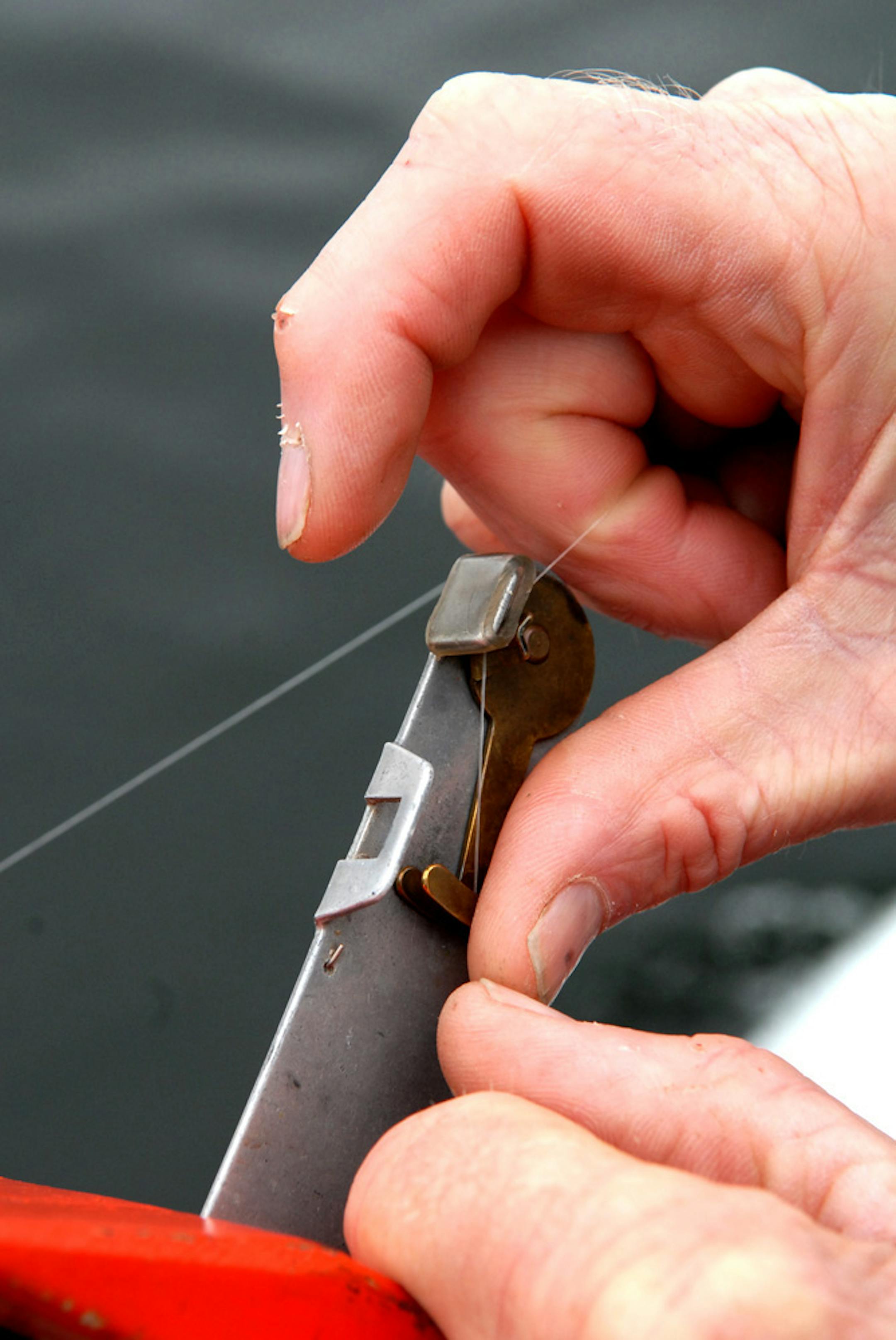 Gary Gehrman runs his monofilament line through the planing board's clip-on mechanism. When a fish strikes and a lure is set by the angler, the mechanism releases and the planing board is set free to be picked up later. Some planing boards stay on the line when a fish is hooked, and are retrieved with the fish.