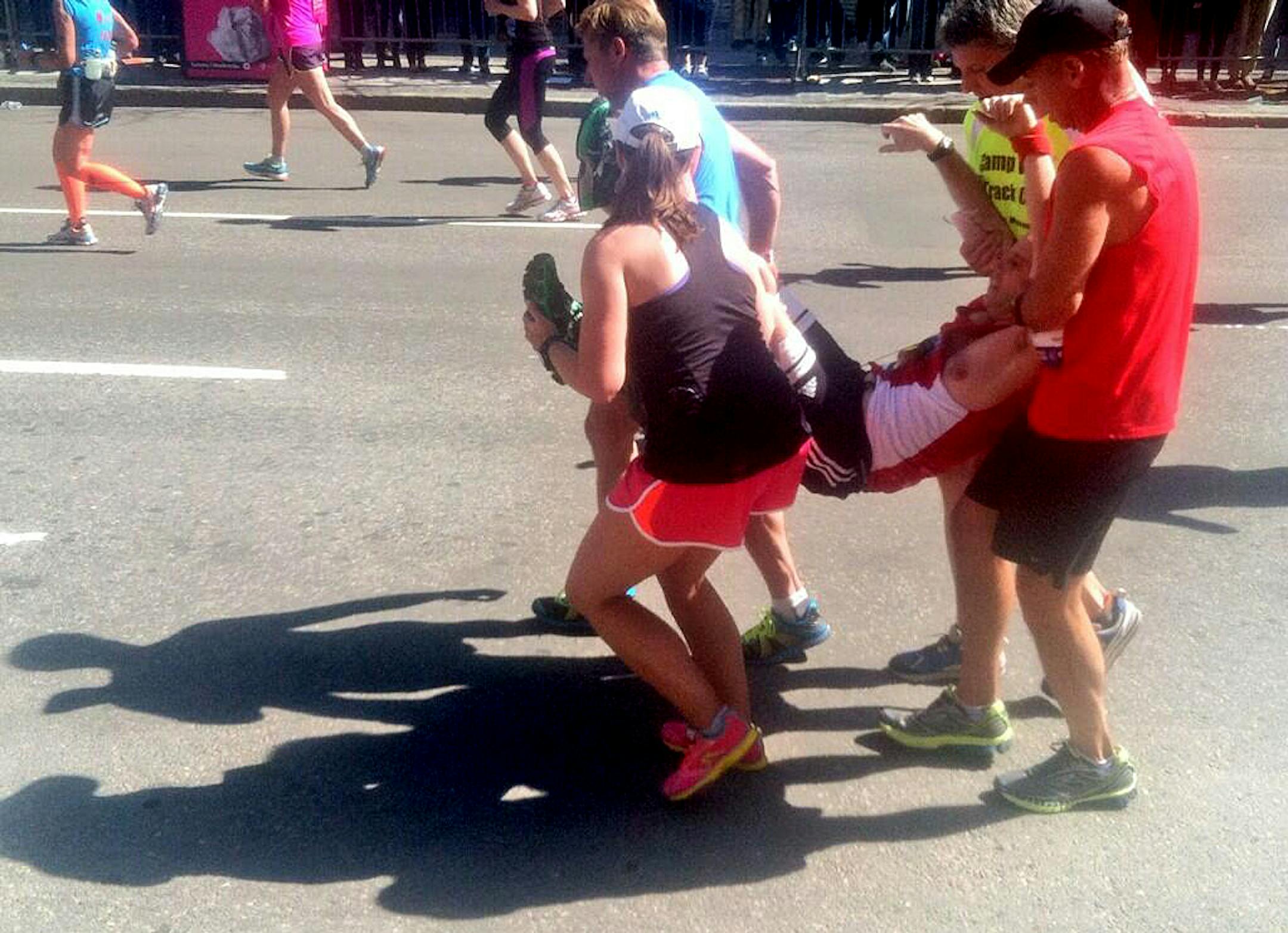 Runners carry a fellow participant near the 26-mile mark of the Boston Marathon, and help him cross the finish line, Monday, April 21, 2014, in Boston. (AP Photo/The Washington Post, Wesley Lowery) WASHINGTON TIMES OUT; NEW YORK TIMES OUT;THE WASHINGTON EXAMINER AND USA TODAY OUT; MAGS OUT; NO SALES