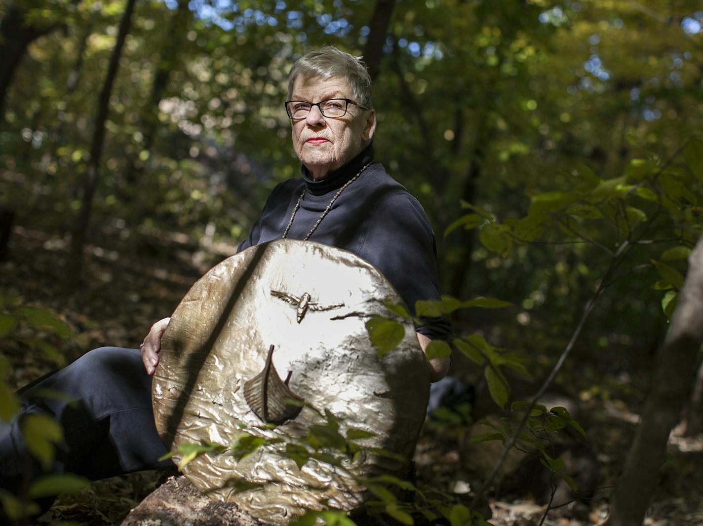 Artist Nancy Randall sits with a bronze shield she created at her home in Hopkins October 10, 2014. Randall's upcoming retrospective at Saint John's University in Collegeville will feature many similar works laid or partially buried outdoors in a woodland setting. The ever-changing light and elements of nature point to a theme of continual transformation. (Courtney Perry/Special to the Star Tribune)