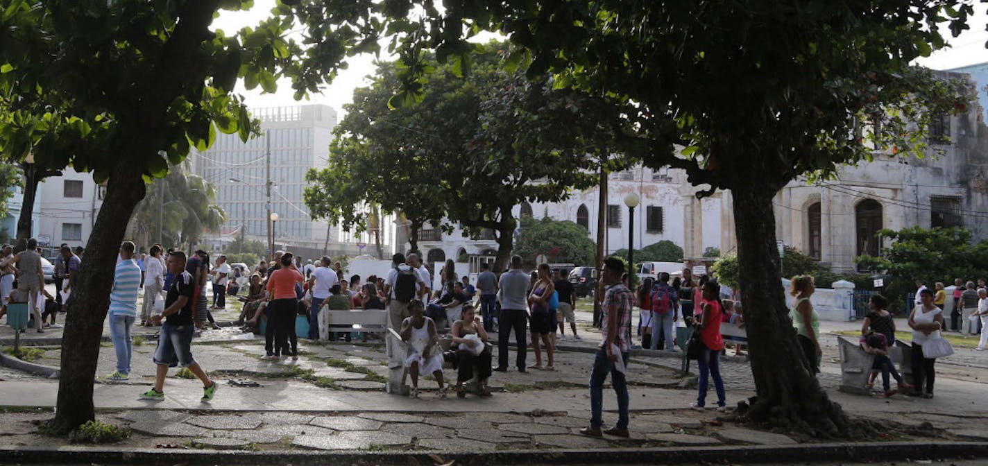 People applying for U.S. visas wait in a park near the U.S. Interests Section, left in background, in Havana, Cuba, Wednesday, July 1, 2015. President Barack Obama announced on Wednesday that the U.S. and Cuba will reopen their embassies in Havana and Washington, heralding a "new chapter" in relations after a half-century of hostility. The posts are scheduled to open July 20, Cuba's Foreign Ministry said. (AP Photo/Desmond Boylan)