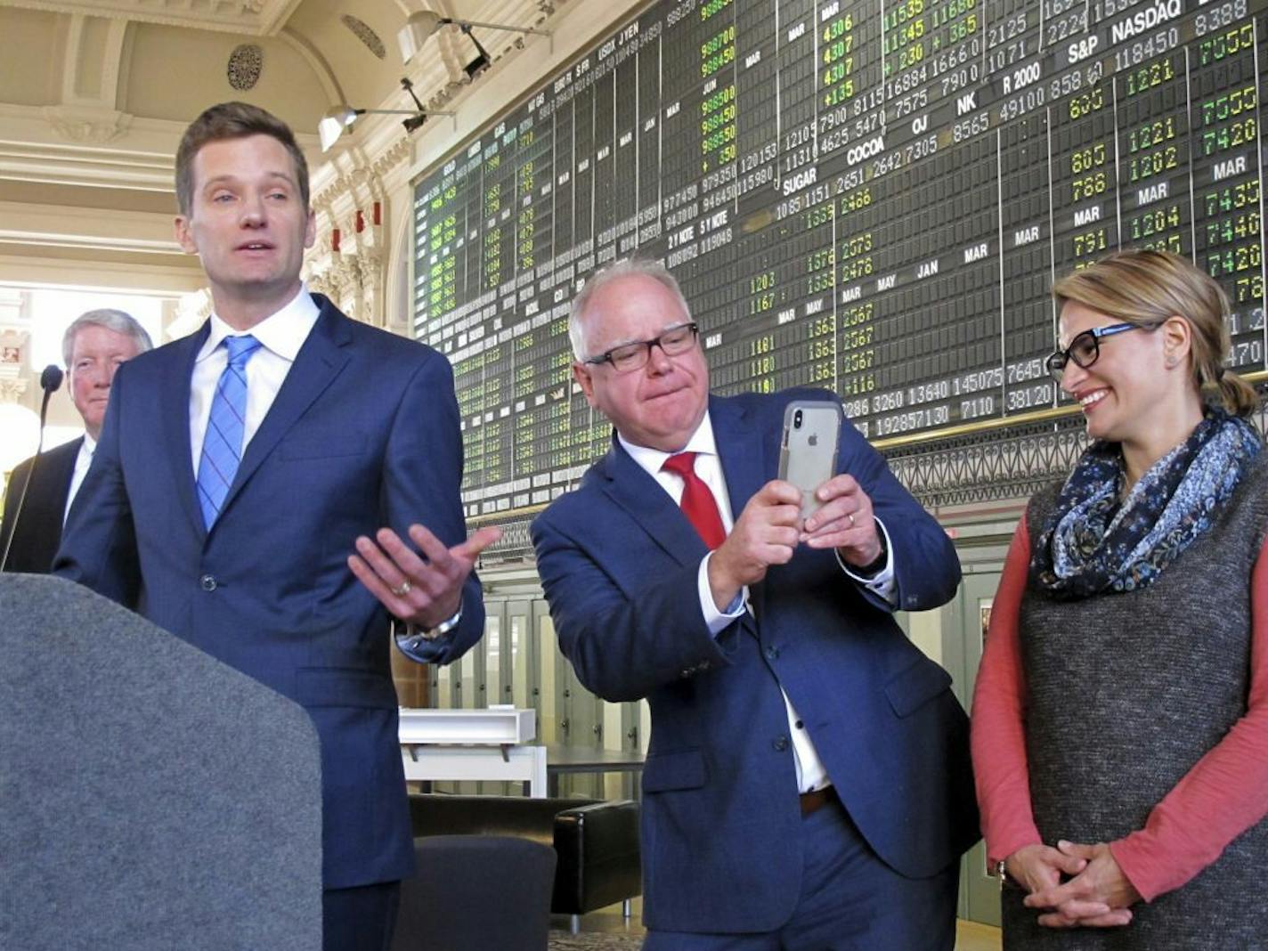 Minnesota Gov.-elect Tim Walz, center, leans to get a picture of the wife and children of Steve Grove, left, Walz's new commissioner of economic development, Friday, Jan. 4, 2019, at the Grain Exchange in Minneapolis. Walz named seven more agency heads at the event. At right is Lt. Gov.-elect Peggy Flanagan.