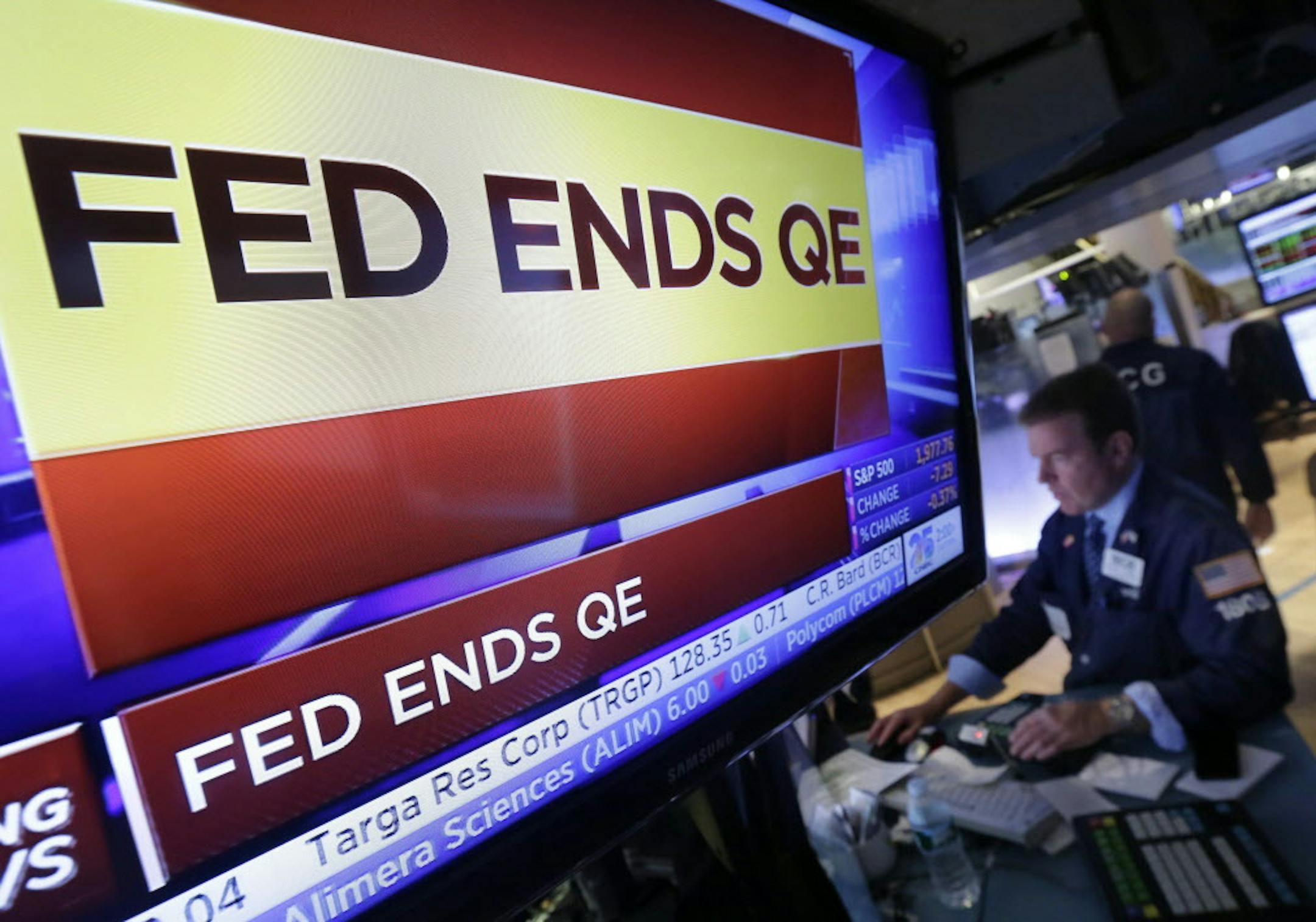 Specialist Michael O'Mara works at his post on the floor of the New York Stock Exchange, as a television screen shows the decision of the Federal Reserve, Wednesday, Oct. 29, 2014. The Fed plans to keep a key interest rate at a record low to support a U.S. job market that's improving but still isn't fully healthy and help lift inflation from unusually low levels. As expected, it's also ending a bond purchase program that was intended to keep long-term rates low. (AP Photo/Richard Drew)