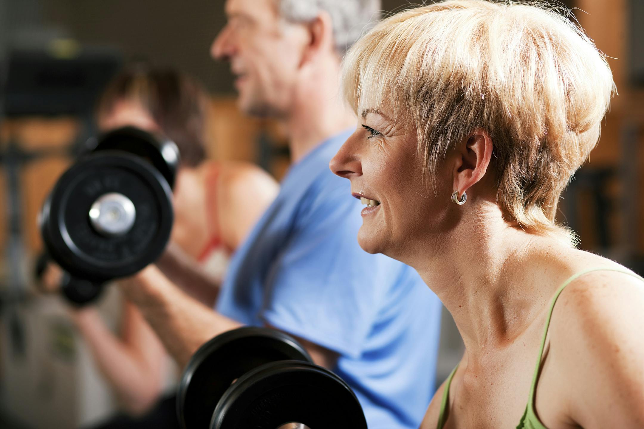 Three senior people - two women and one man - in the gym lifting dumbbells, exercising. istock