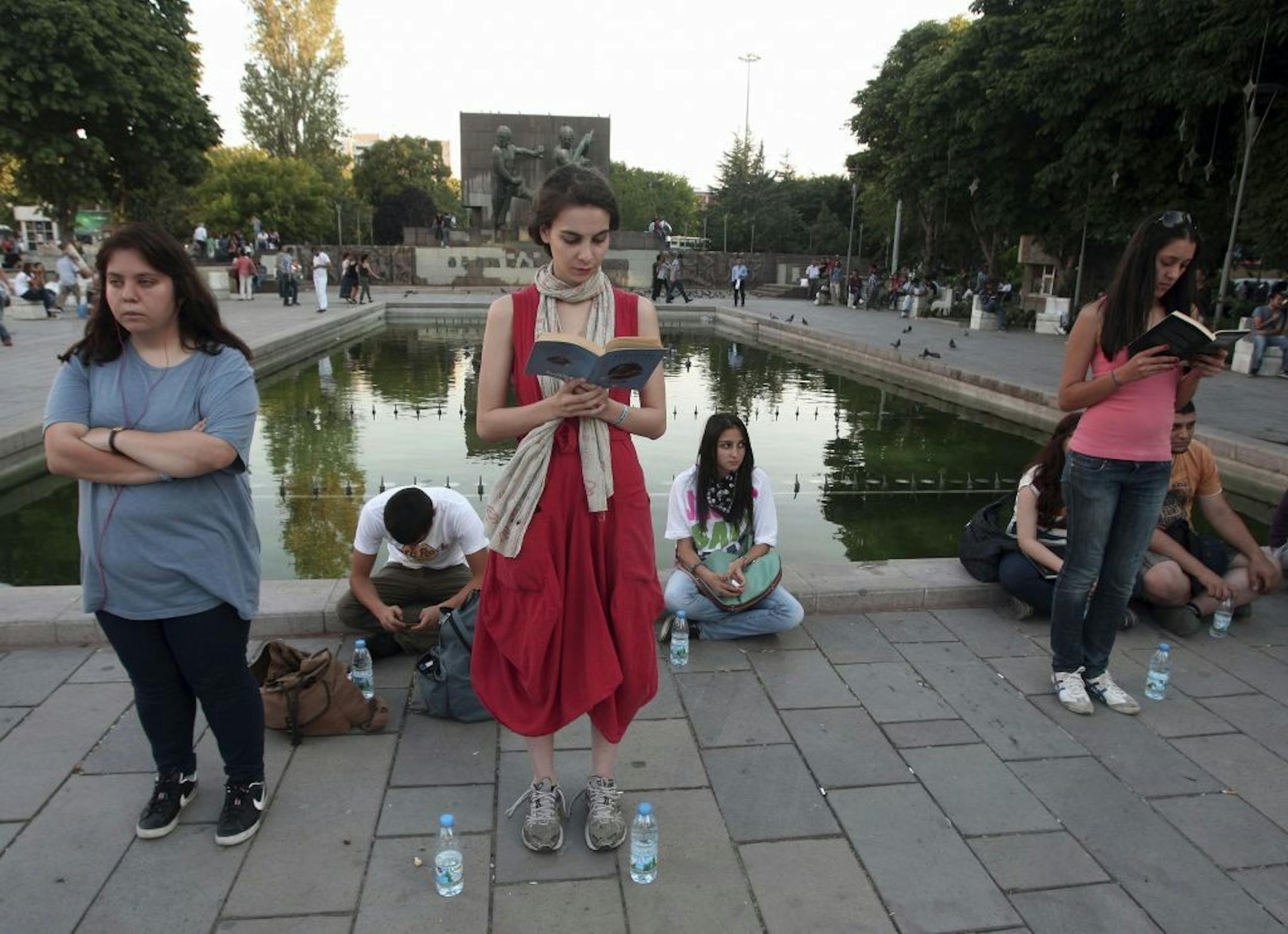 In this photo taken Tuesday, June 18, 2013, a woman stands in a silent protest as others read at Kizilay Square in Ankara, Turkey.
