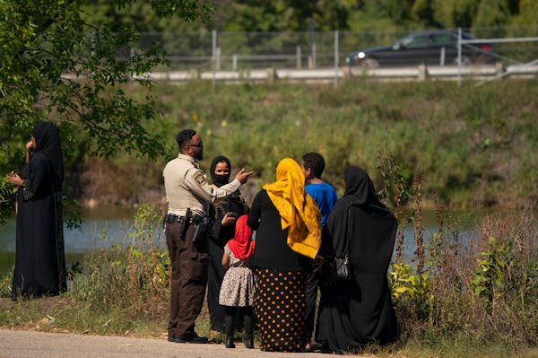 A Hennepin County Sheriff's Deputy stood with community members at the edge of a pond in Rosland Park in Edina where the body of child was recovered T