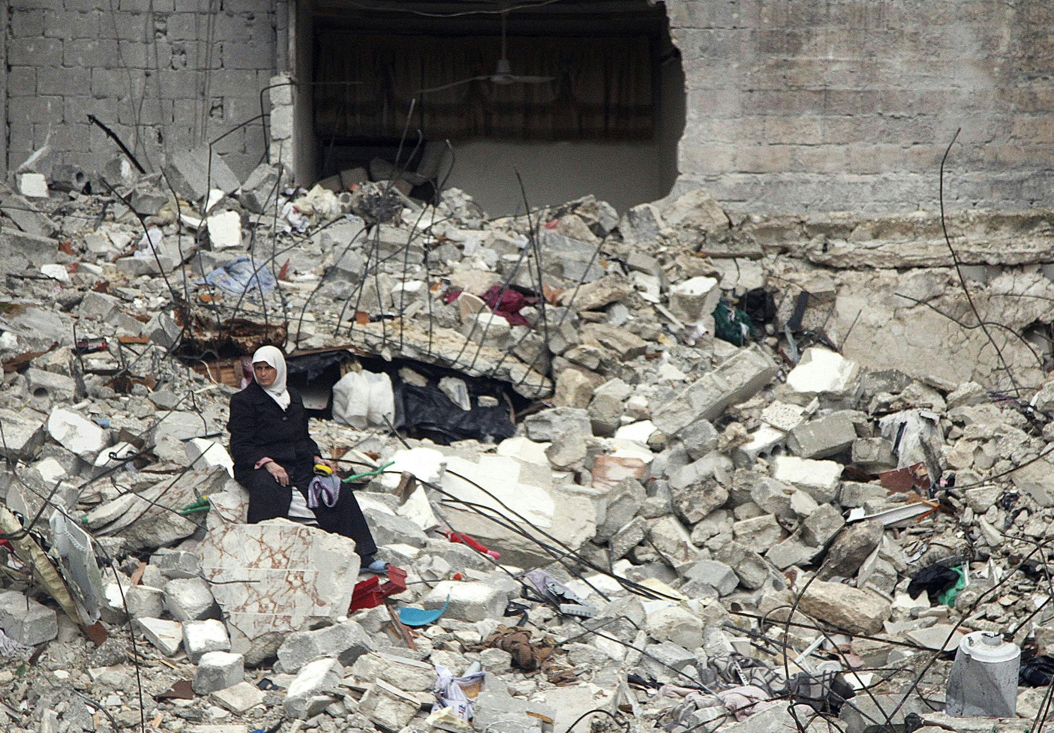 In this Thursday, Feb. 6, 2013 photo, a Syrian woman sits on the ruins of her house, which was destroyed in an airstrike by government warplanes a few days earlier, killing 11 members of her family, in the neighborhood of Ansari, Aleppo, Syria.