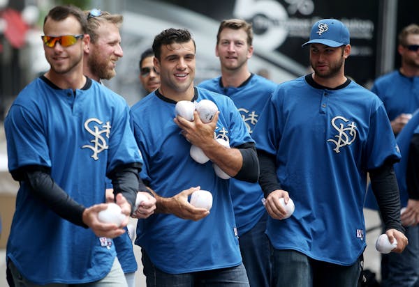 St. Paul Saints catcher Vincent DiFazio, center, is loaded down with soft baseballs that Saints players gave out to passersby before the start of the 