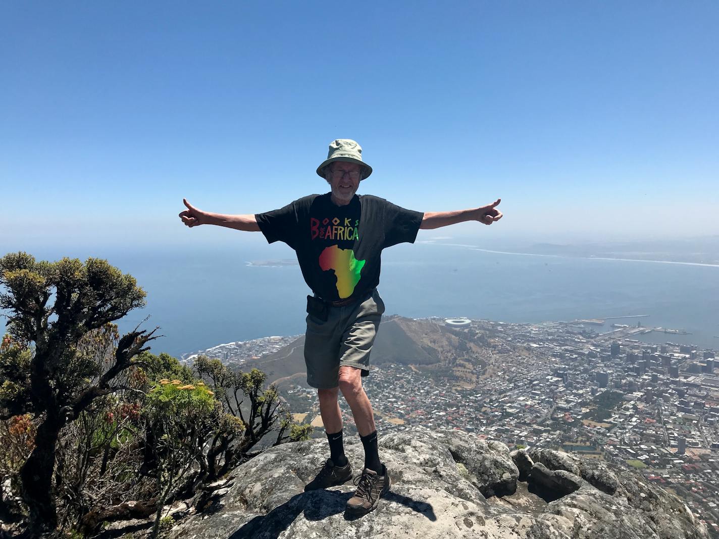 Books for Africa founder Tom Warth standing on a rock with a view of a city and body of water in the background.