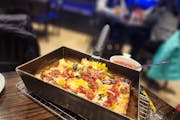 A rectangular pan holding a pizza with vegetables and dollops of sauce on it, on a table in a brewpub