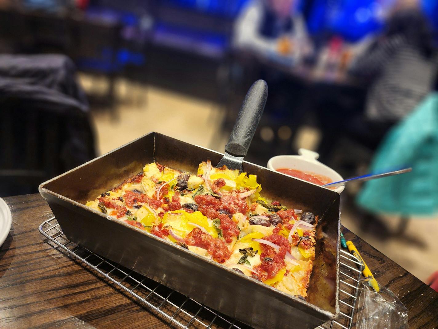 A rectangular pan holding a pizza with vegetables and dollops of sauce on it, on a table in a brewpub