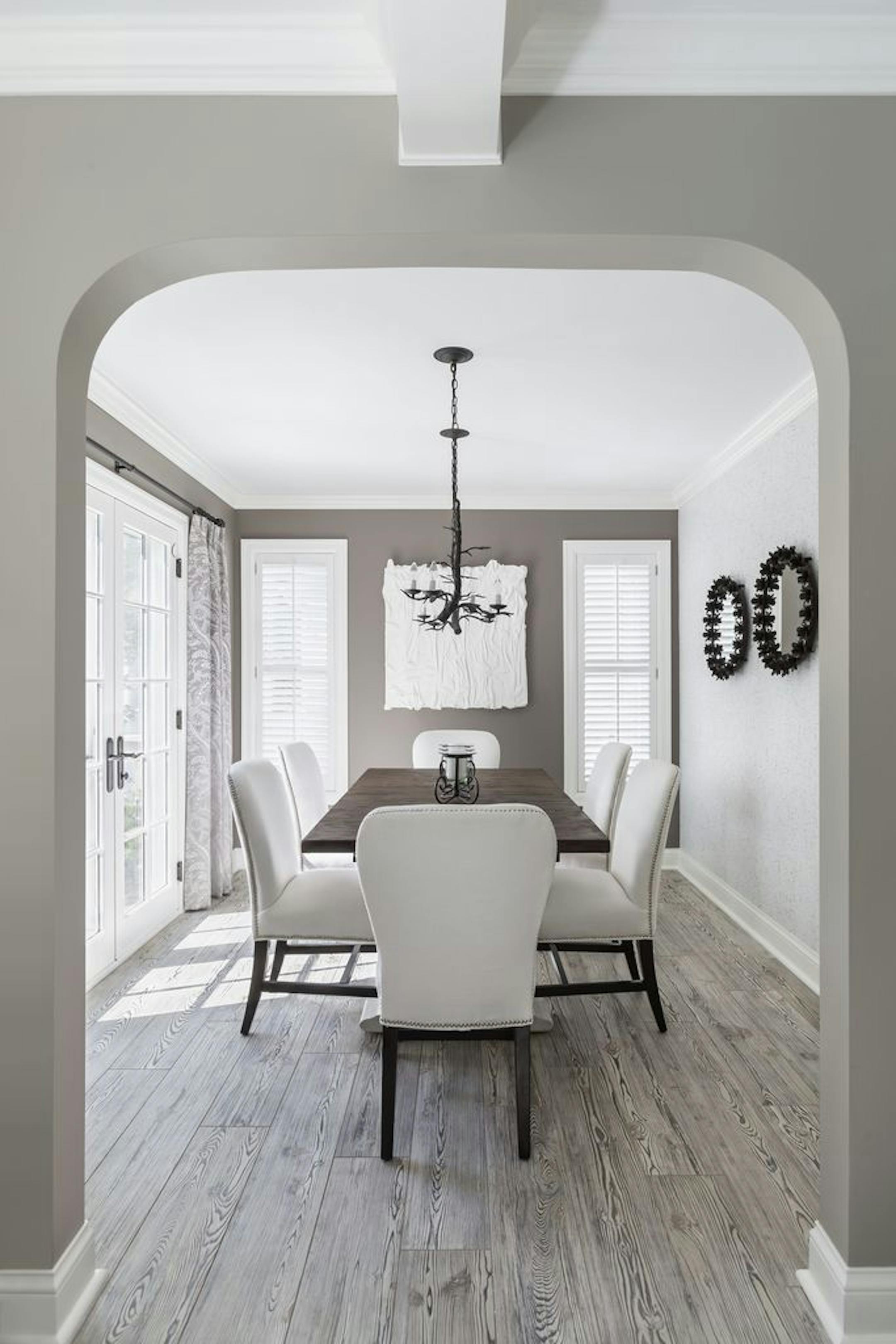 The new formal dining room is dressed up with a bronze twig-shaped chandelier, petal mirrors and birch-look wallpaper next to deep taupe walls. The weathered wood-look tile floor matches the flooring in the new kitchen.