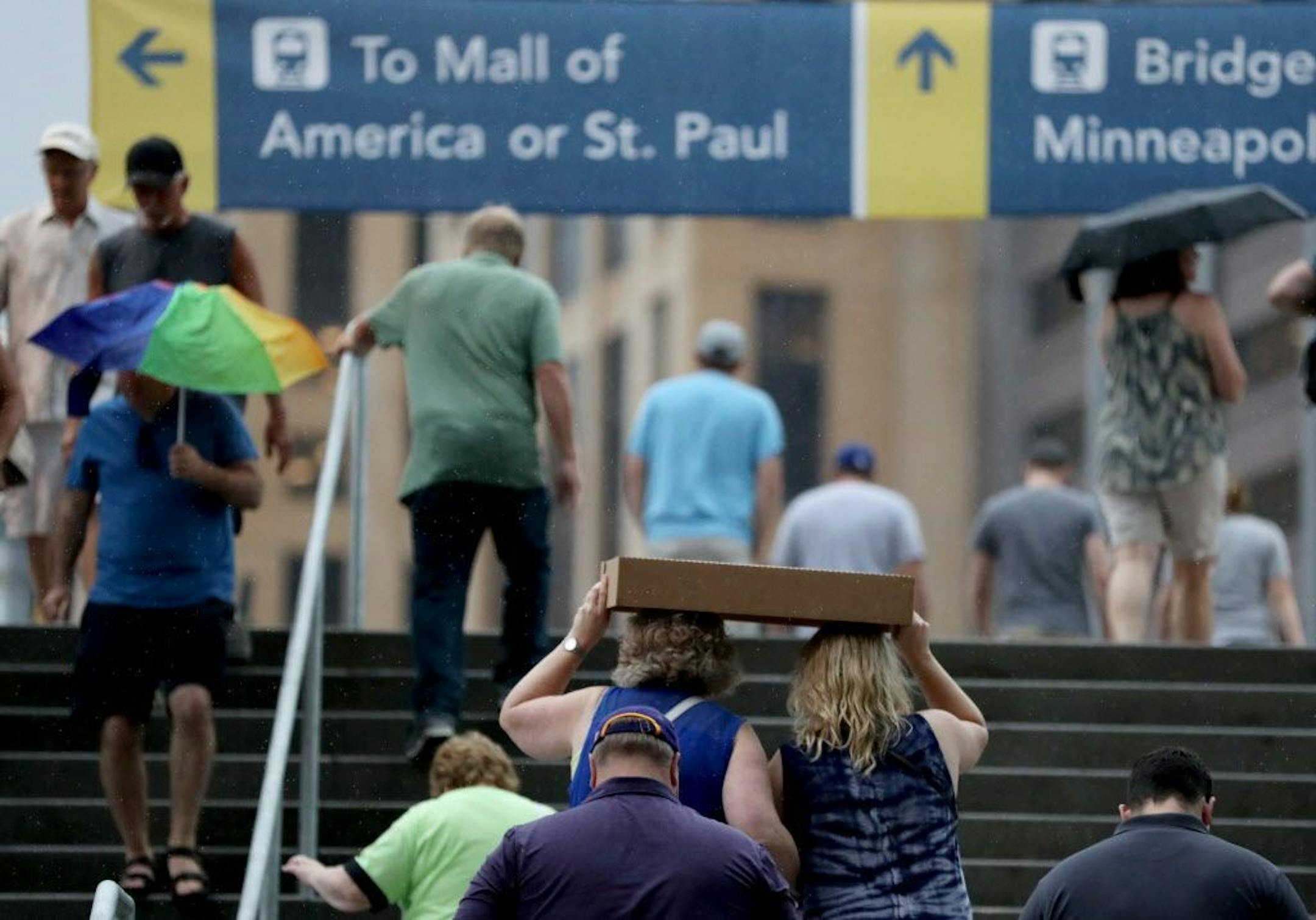Umbrellas and cardboard boxes were used to project fans from the rainy weather during a storm at the public opening at the U.S. Bank Stadium Saturday morning.