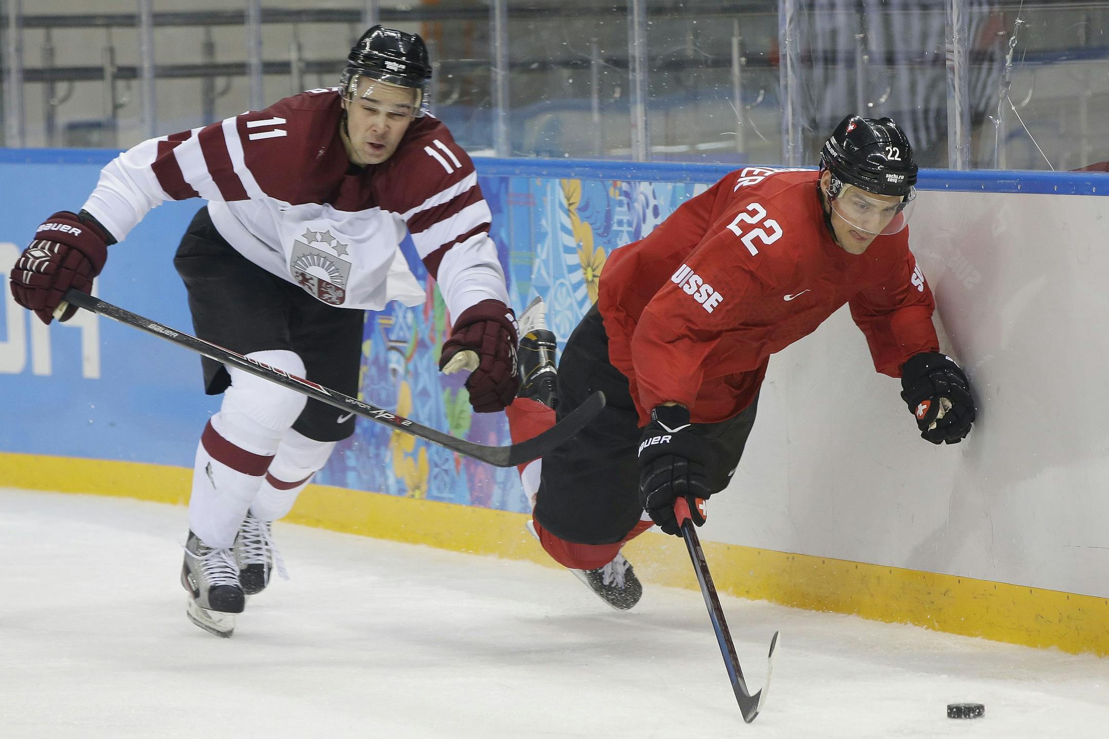 Latvia defenseman Kristaps Sotnieks and Wild forward Nino Niederreiter, who played for Switzerland, chase a loose puck during the third period of a game in the 2014 Olympics.