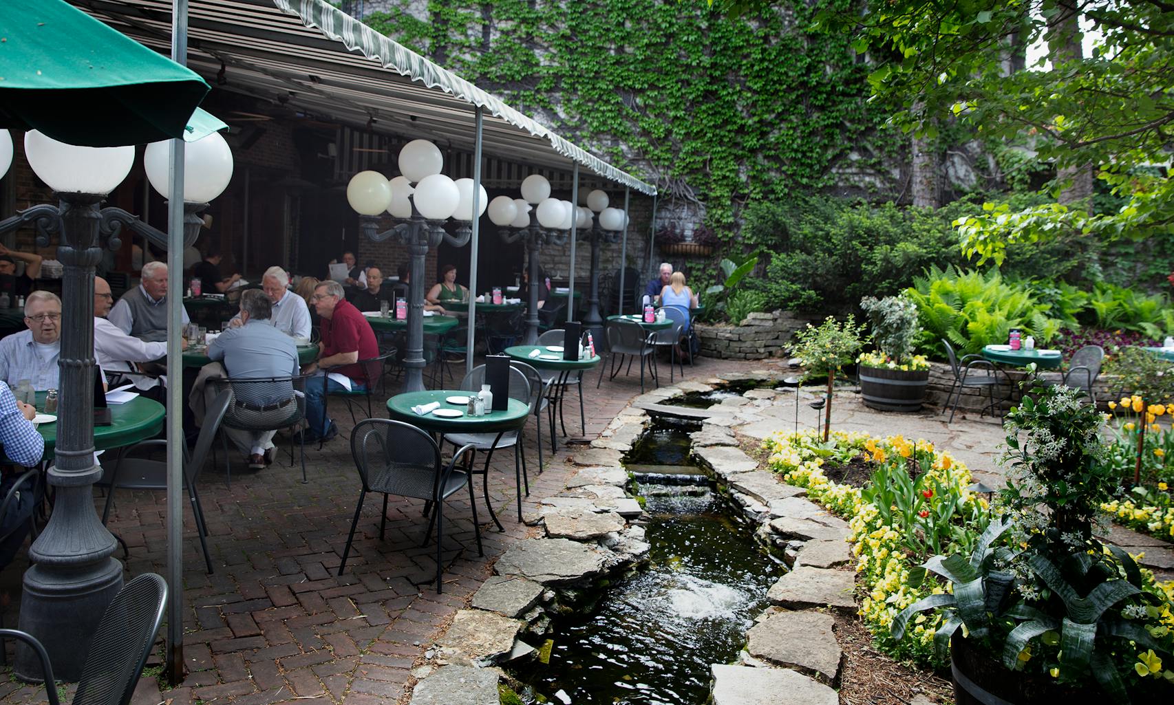 Jax Cafe in northeast Minneapolis. A patio garden, with a stream, a water wheel, flowers, a tented seating area. [ Sidewalks Cafe’s Photos by Rick Nelson