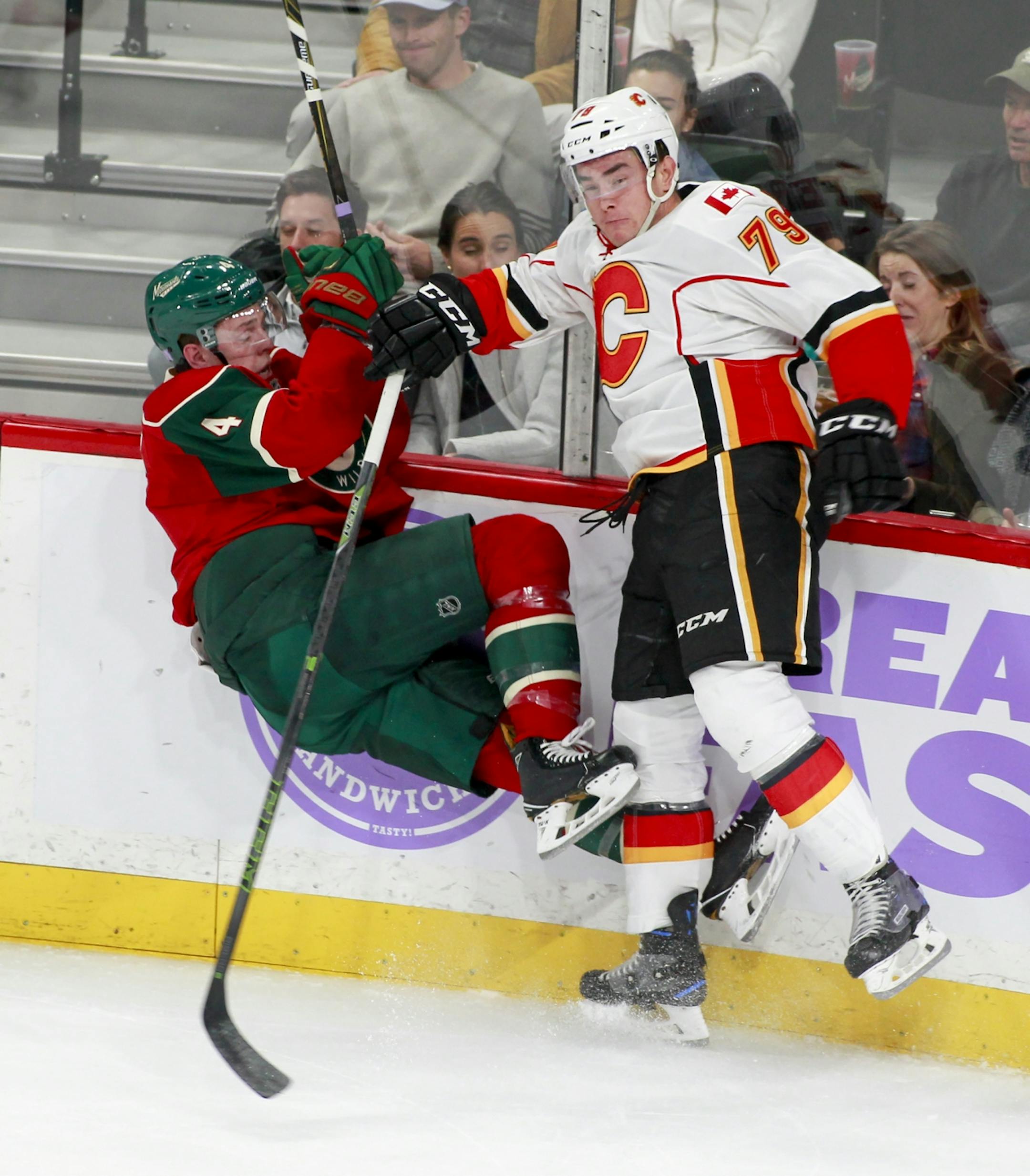 Minnesota Wild defenseman Mike Reilly (4) is checked off the ice by Calgary Flames left wing Micheal Ferland (79) during the first period of an NHL hockey game, Tuesday, Nov. 15, 2016, in St. Paul, Minn.