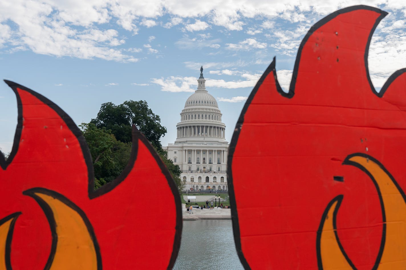 In this Oct. 15, 2021, the U.S. Capitol is seen between cardboard cutouts of flames during a climate change protest near the U.S. Capitol in Washington. President Joe Biden heads to a vital U.N. climate change summit at a time when a majority of Americans regard the deteriorating climate as a problem of high importance to them. That's the finding of a new poll by the Associated Press and the NORC Center for Public Affairs Research and the Energy Policy Institute at the University of Chicago.