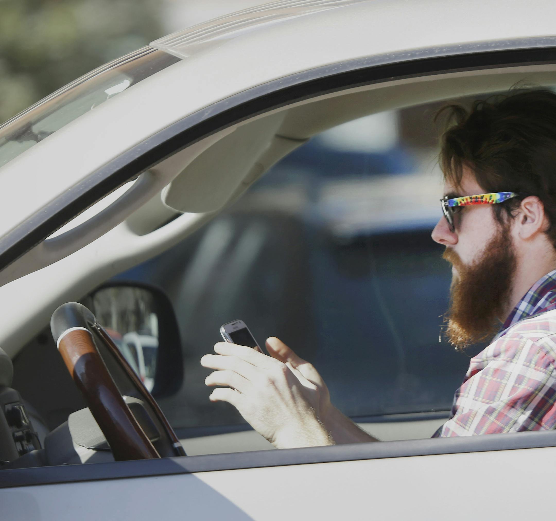 A man works his phone as he drives through traffic.