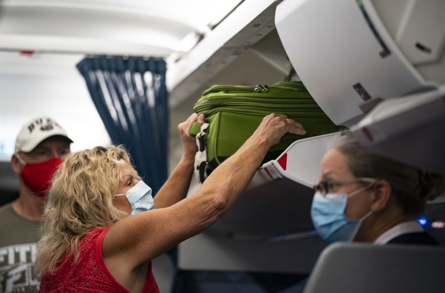 A masked woman placed her luggage in the overhead compartment on a Delta flight.