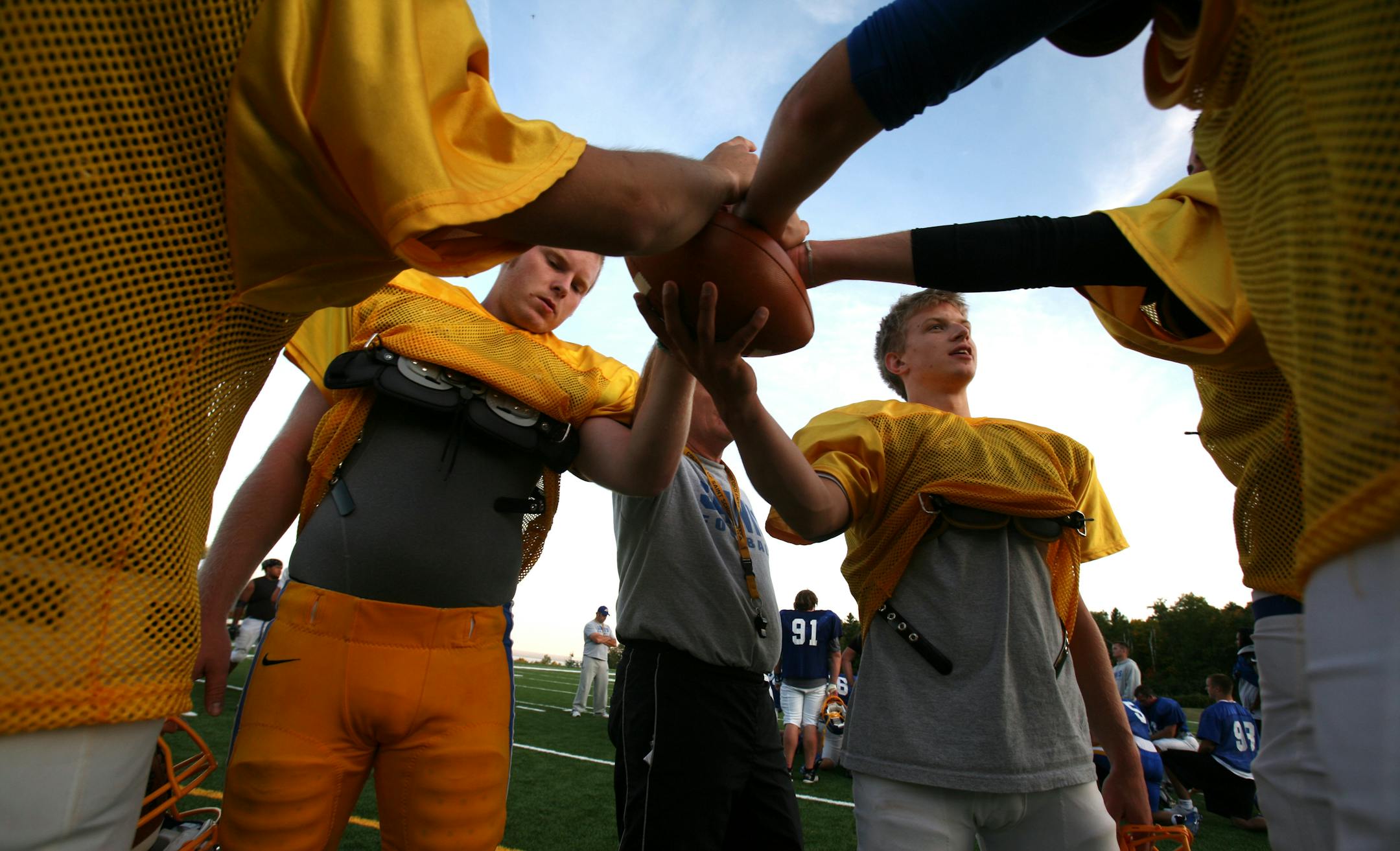 With the football as a centerpiece, a cluster of College of Saint Scholastica players came together for a quiet, unifying moment with their coach at the end of a practice.