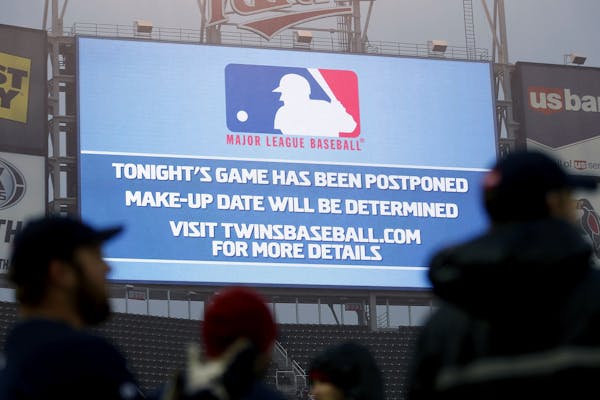 The grounds crew stood in the rain as a game postponement announcement was displayed on the scoreboard at Target Field on Wednesday night. ] CARLOS GO