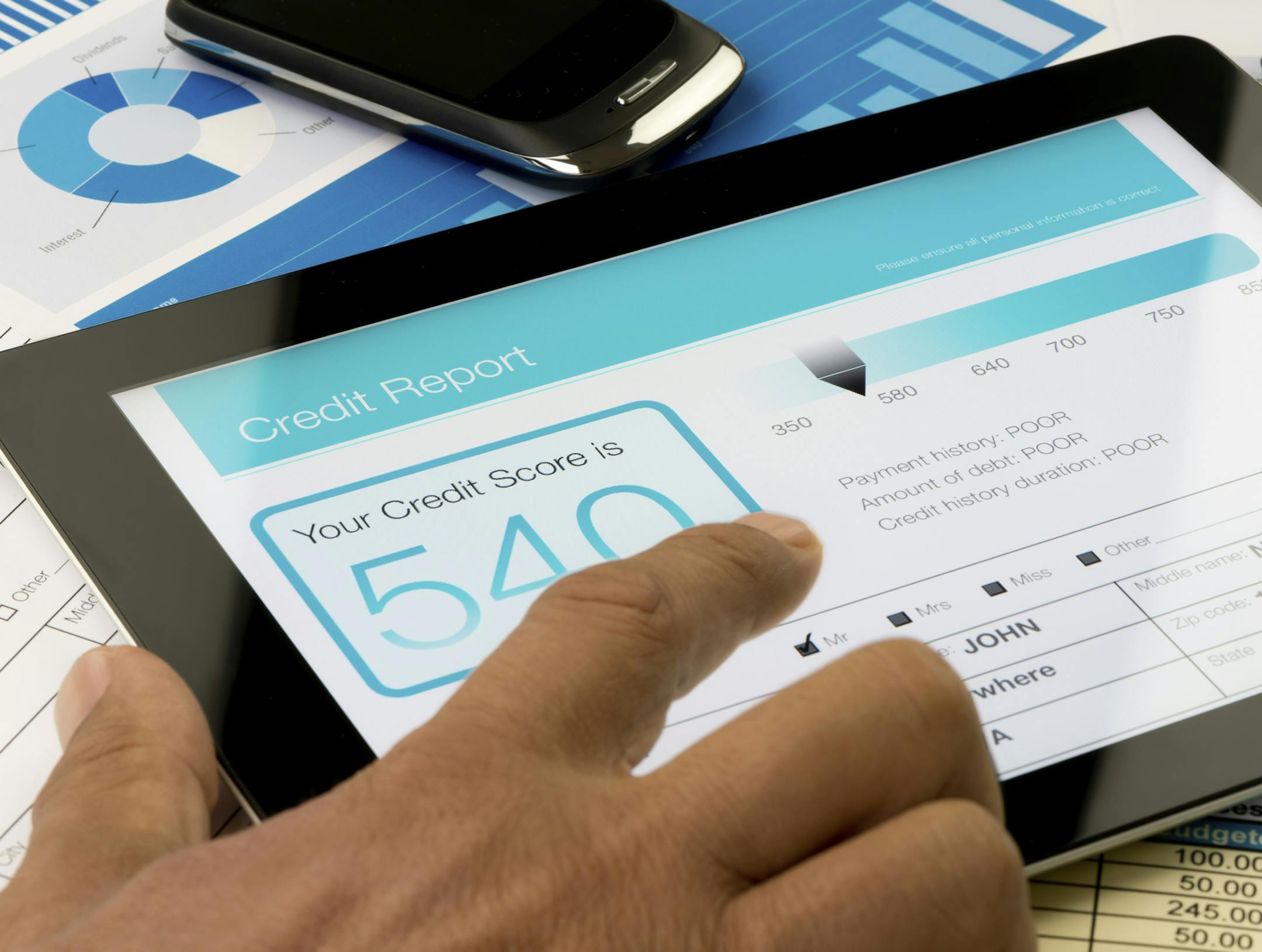 Credit report on a digital tablet with paperwork.