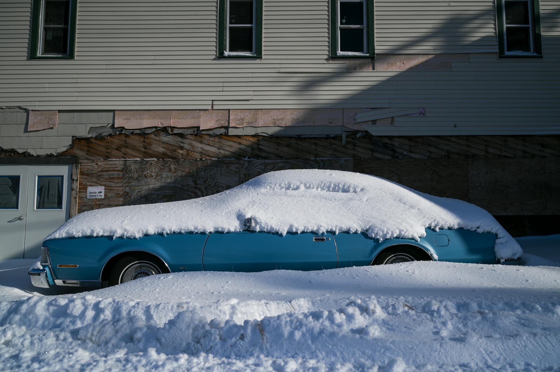 A snow-covered classic car in a downtown alley.